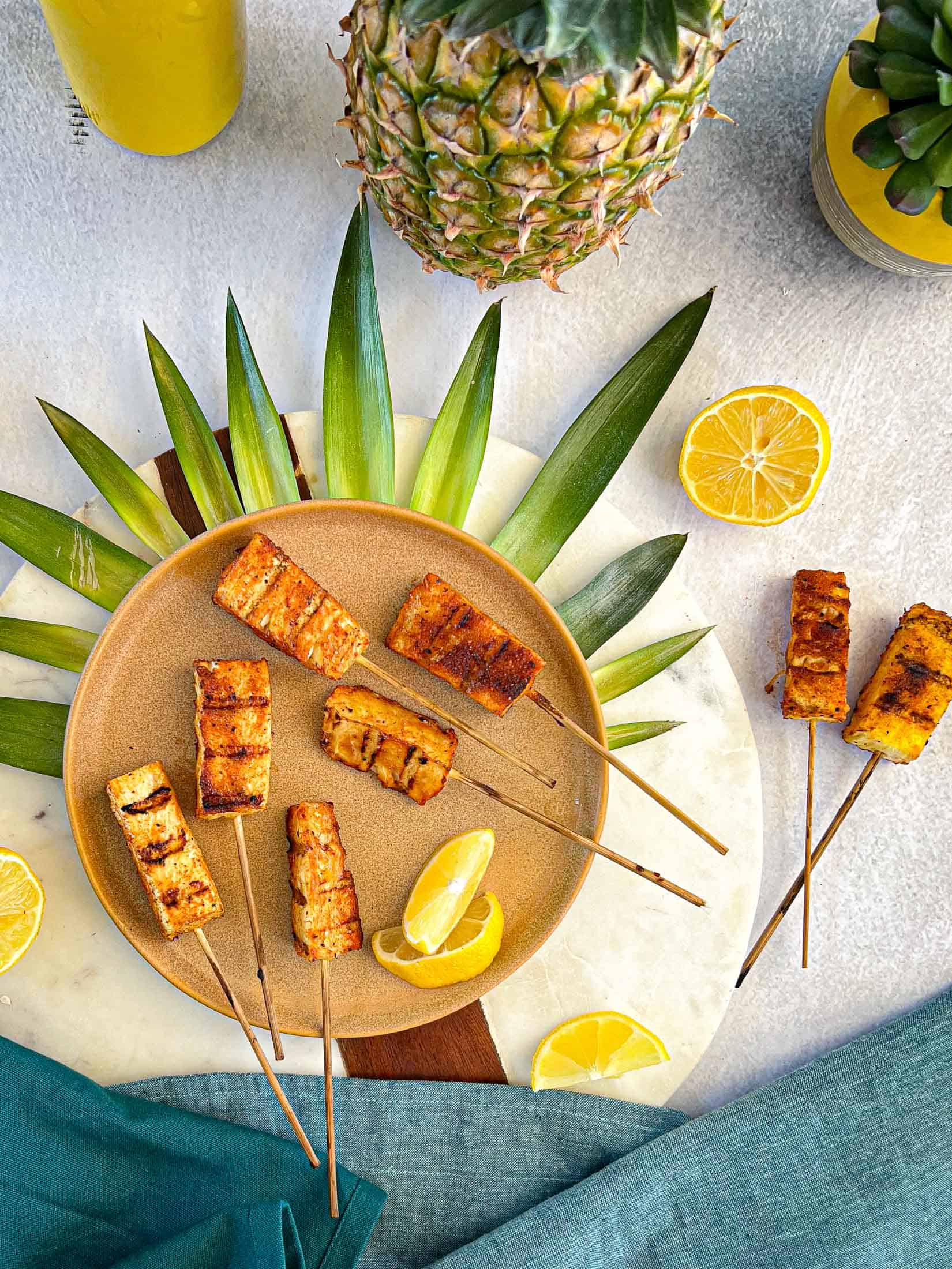 Smoked pineapple on wooden skewers with pineapple leaves and sliced lemons.