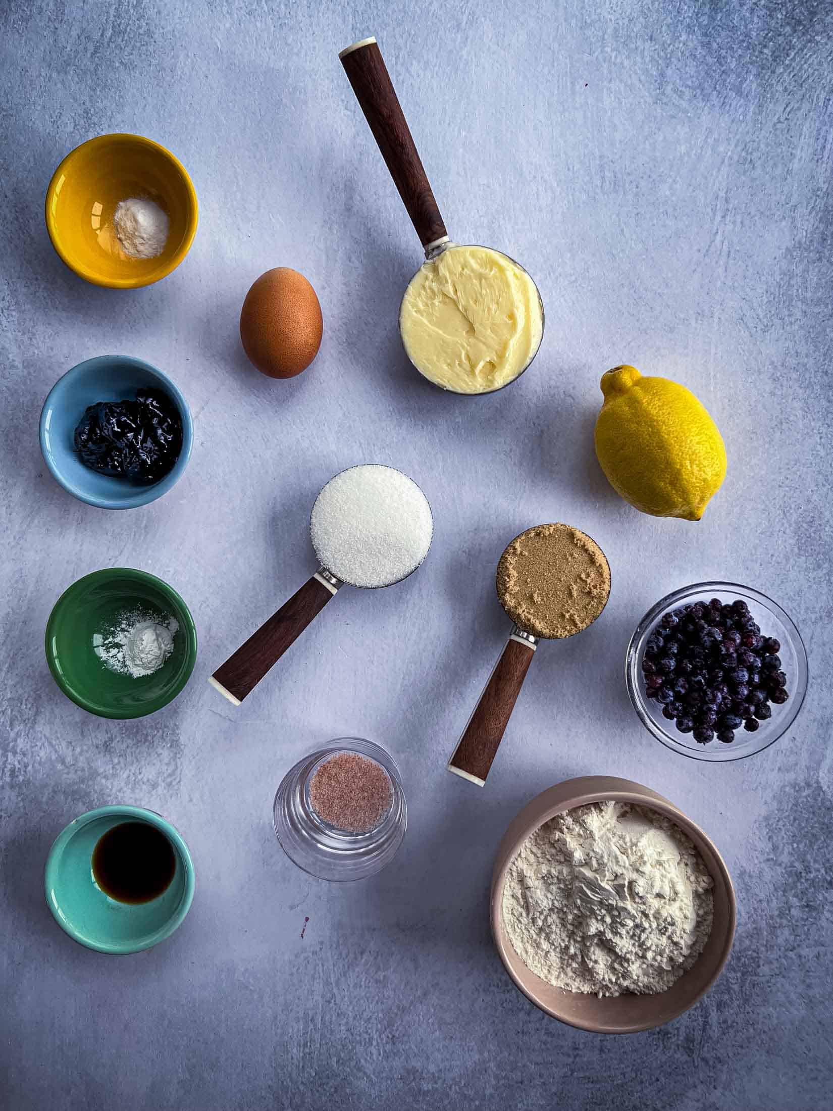 Key ingredients for lemon blueberry cookies with fresh berries, a whole lemon, dry ingredients and wet ingredients.