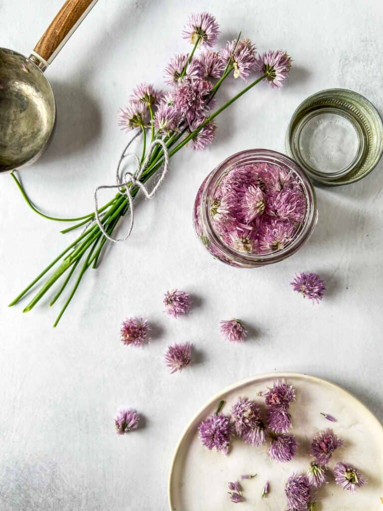 Chive blossoms in a jar of vinegar with tied chives and chives sprinkled around.