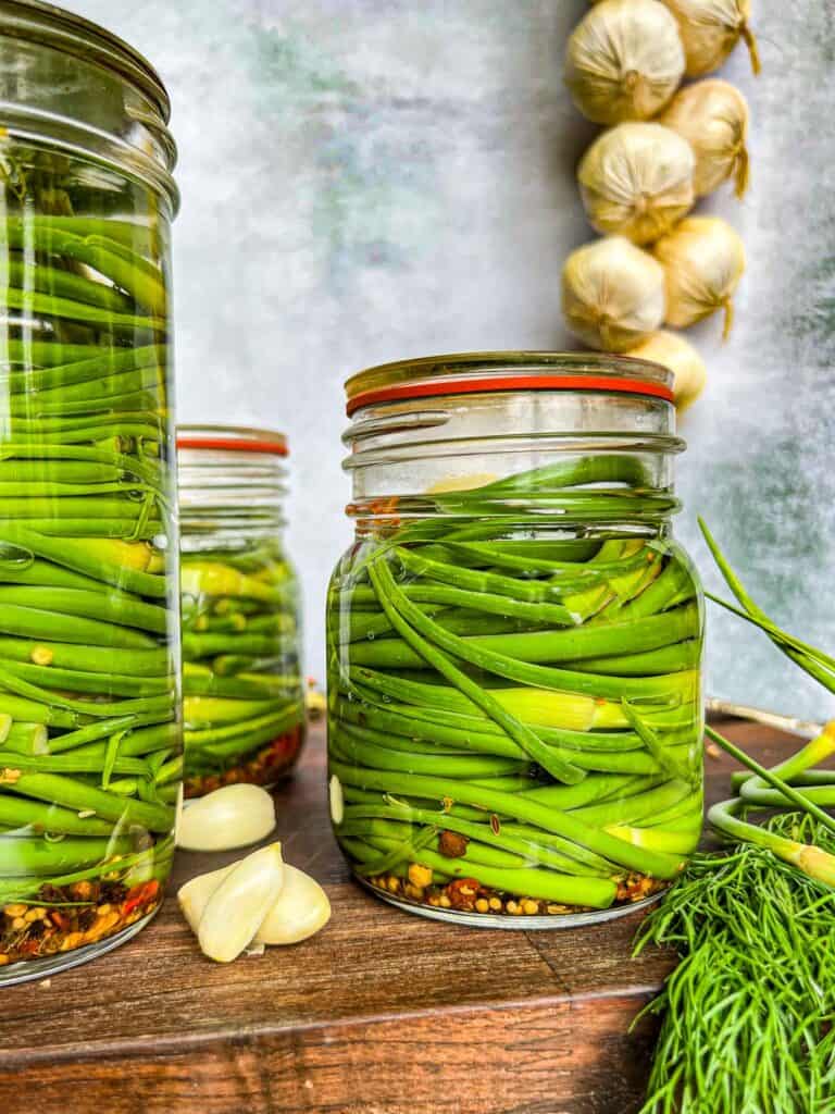 Pickled garlic scapes in clear jars, stacked horizontally.