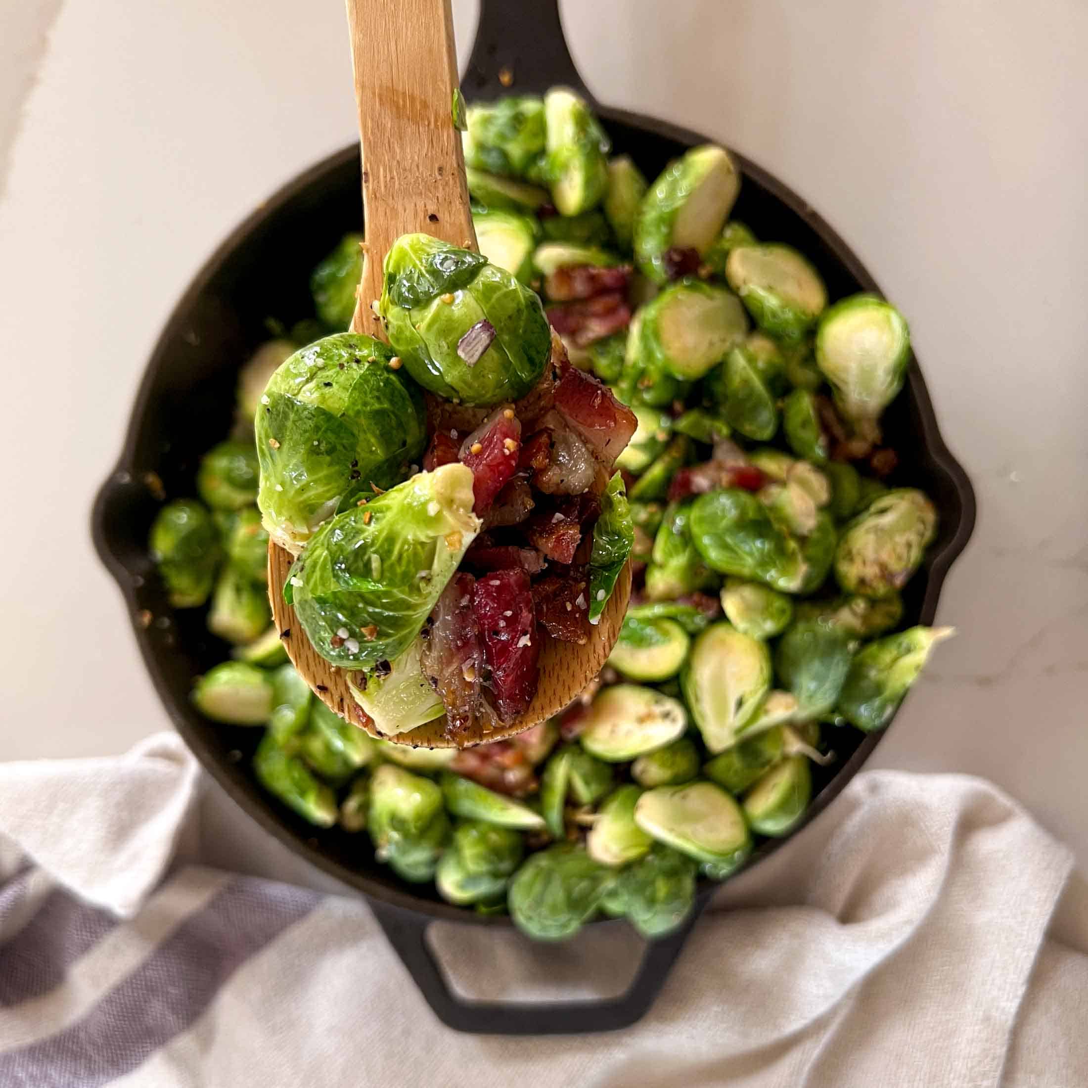 A wooden spoon holding up seasoned, smoked brussels sprouts.