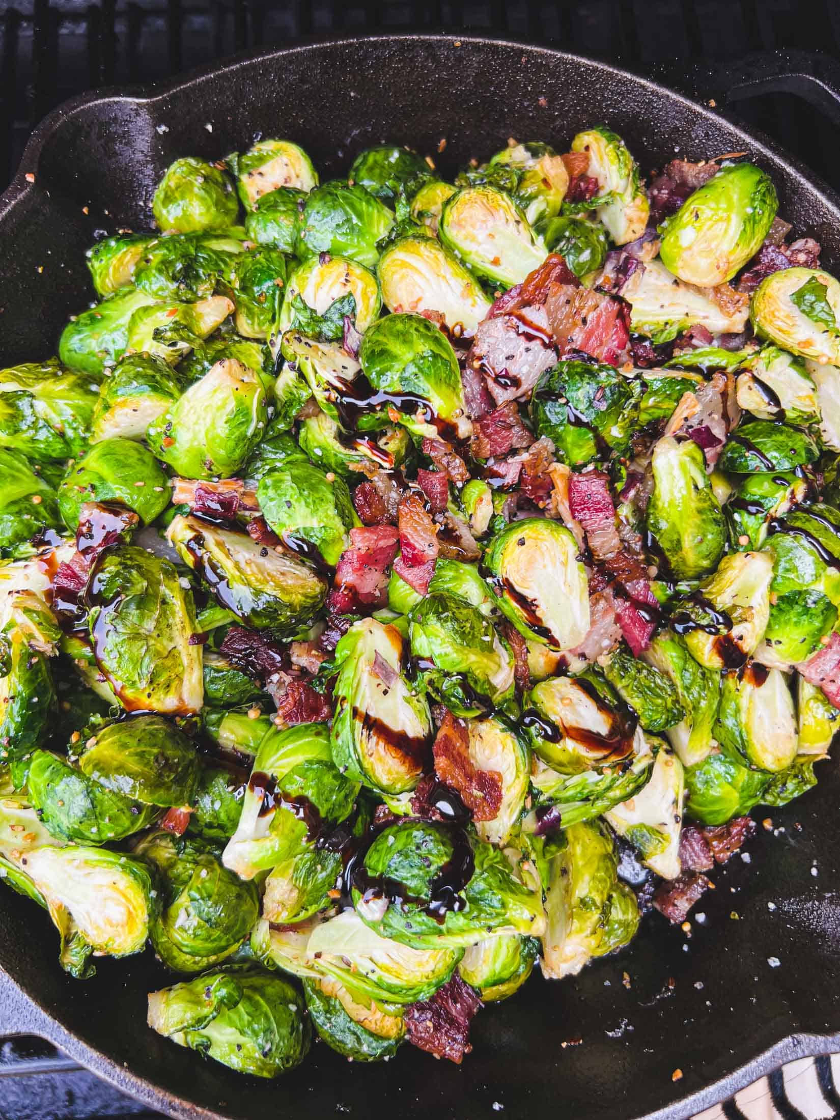Crispy brussels sprouts in a cast iron skillet with balsamic glaze drizzled on top on the smoker.