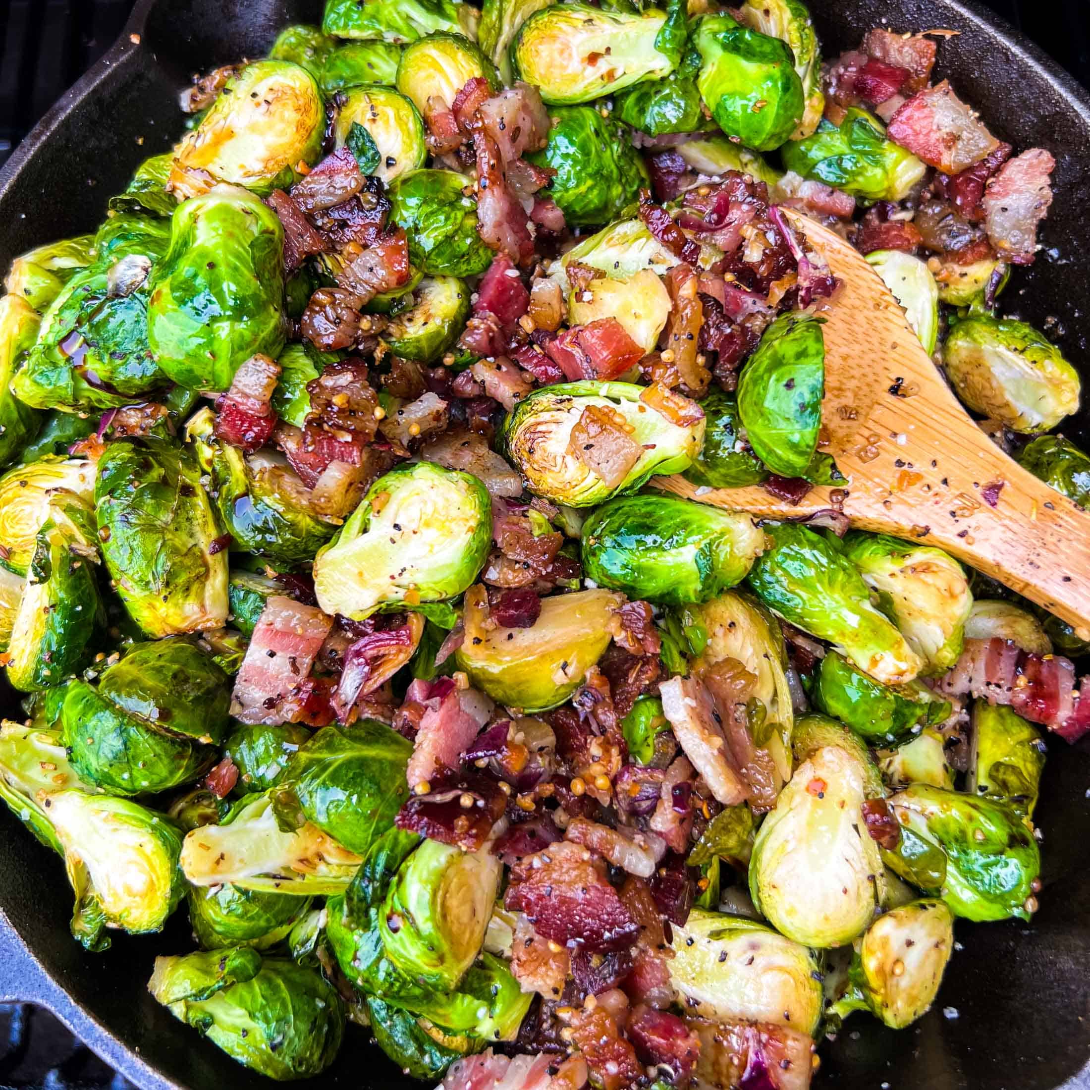 Crispy brussels sprouts in a cast iron skillet with balsamic glaze drizzled on top on the smoker.