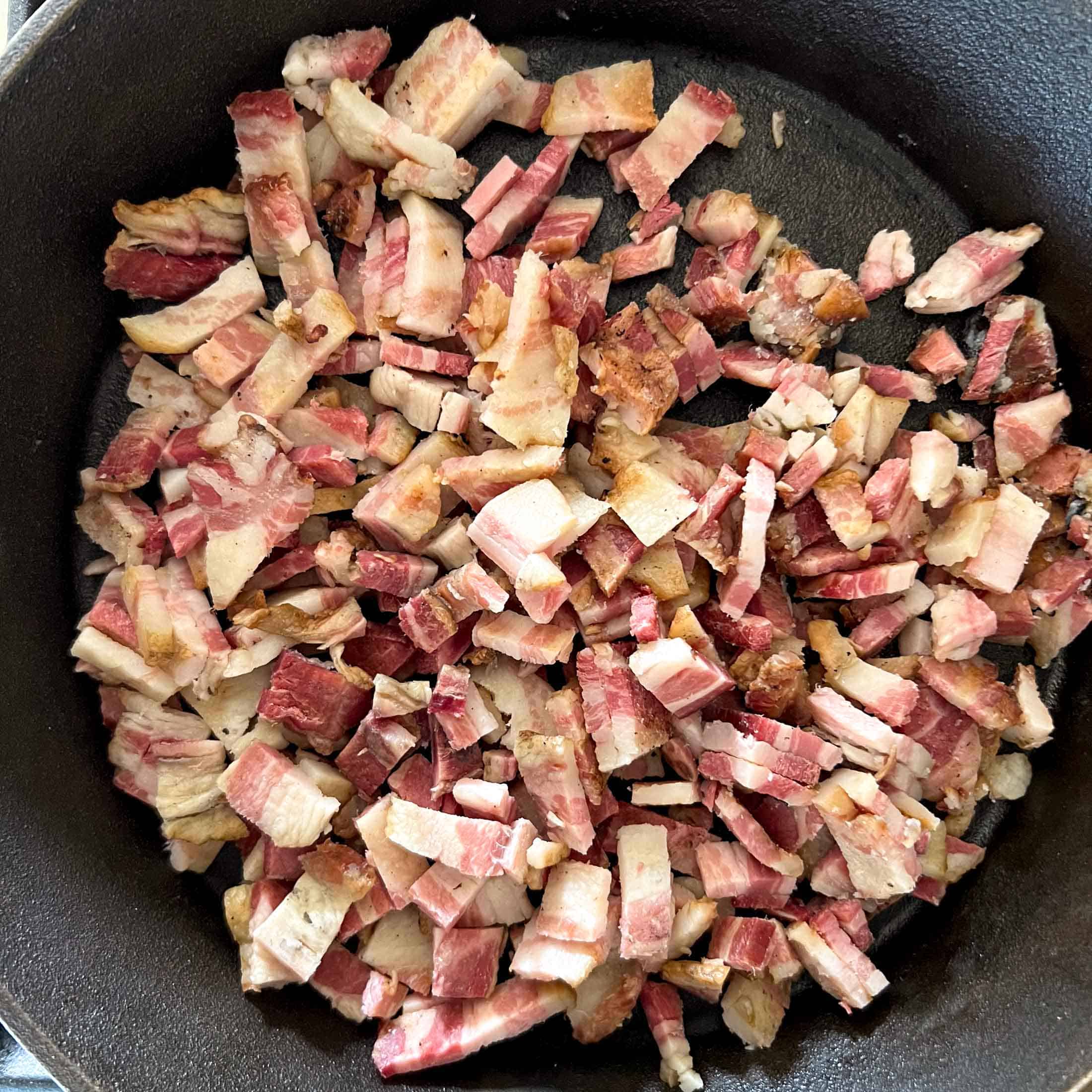 Raw bacon diced in a cast iron pan.