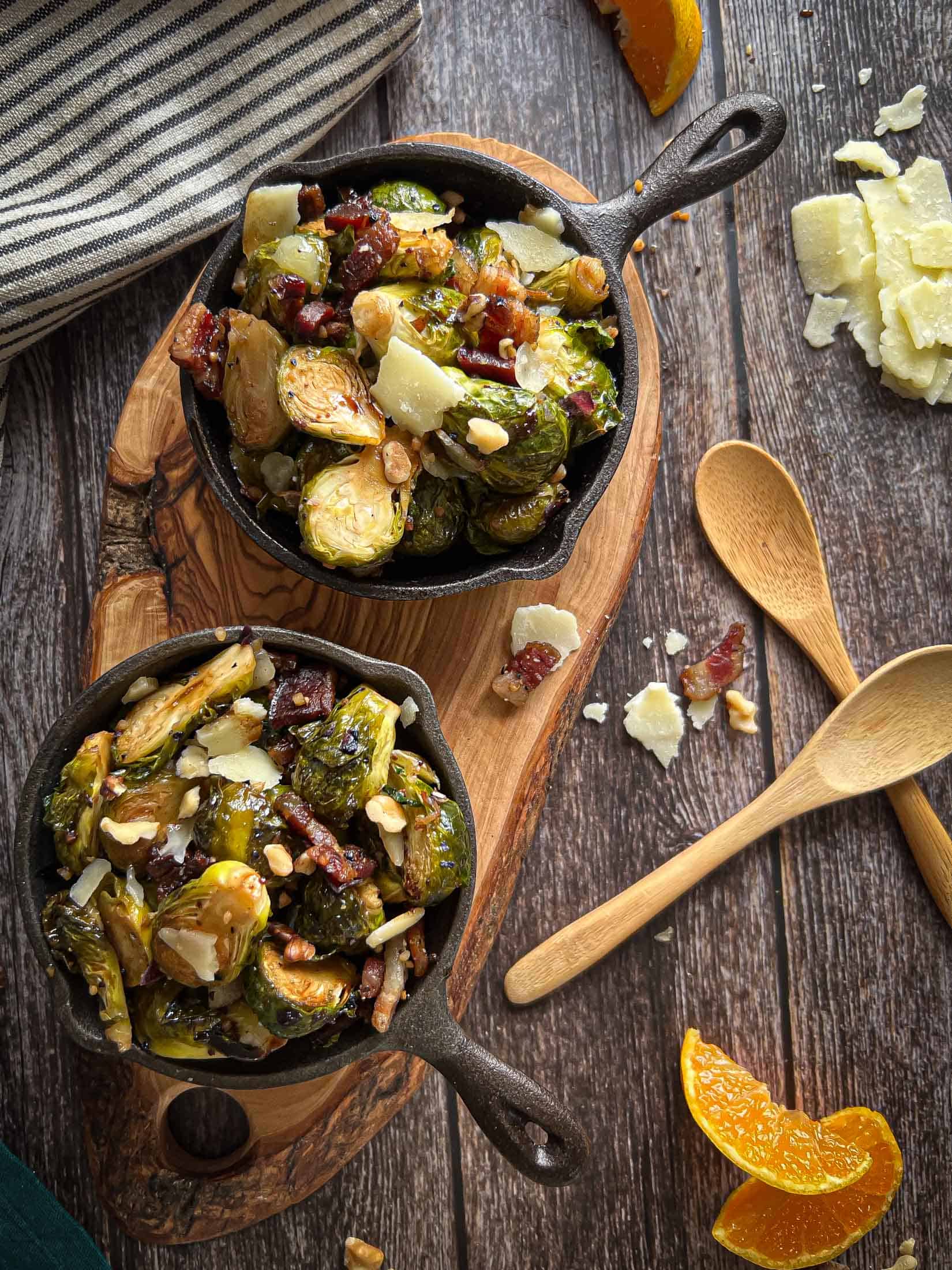Two small cast iron skillets filled with smoked brussels sprouts with parmesan, oranges, and bacon in the foreground.