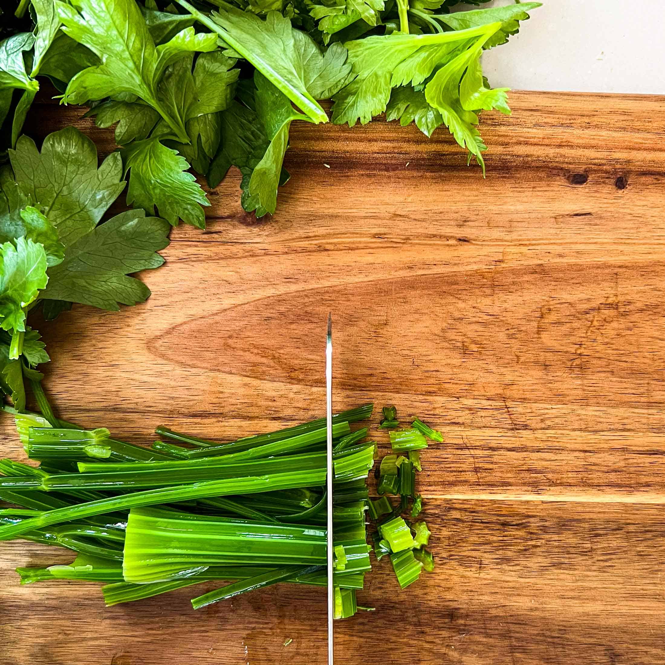 Blanched celery being cut on a wooden cutting board.