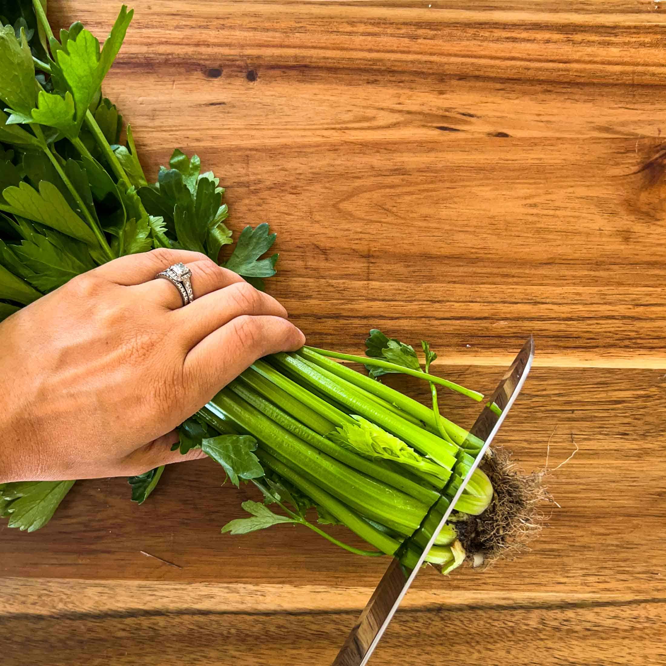 A large chef's knife cutting into a bundle of celery, chopping the bottom portion off.