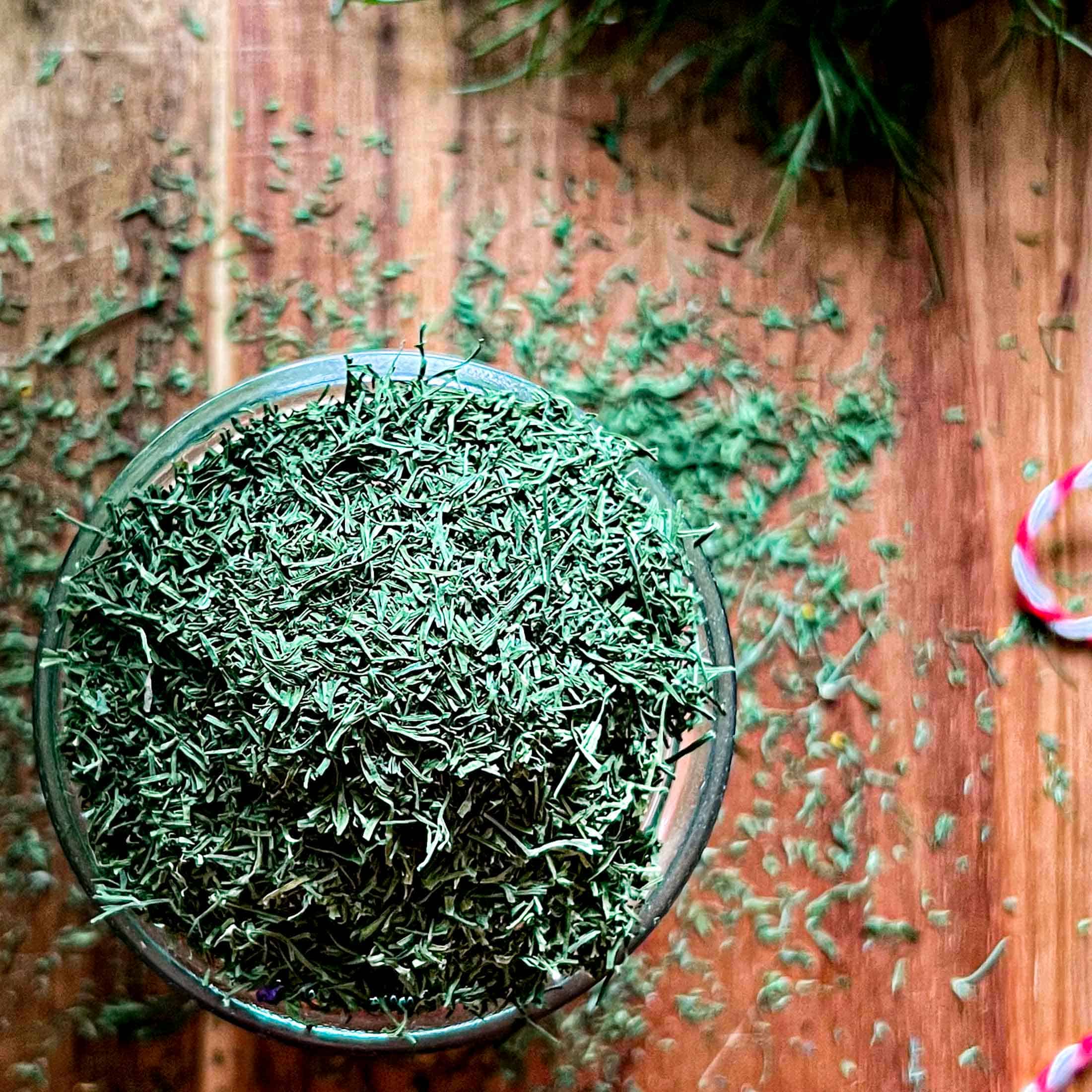 Dry dill flakes in a glass jar, spilling out onto a wooden cutting board.