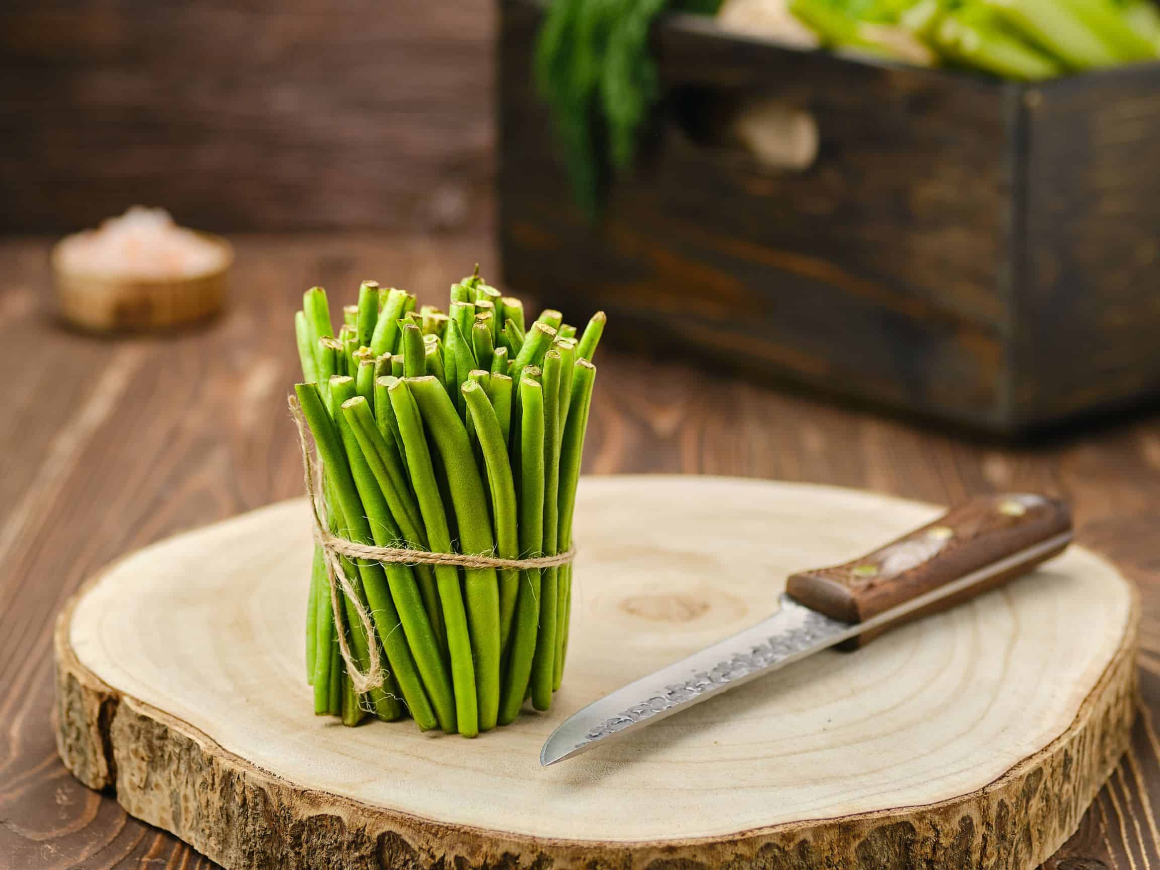 Green beans with the ends cut off on a large wood board with a knife beside.