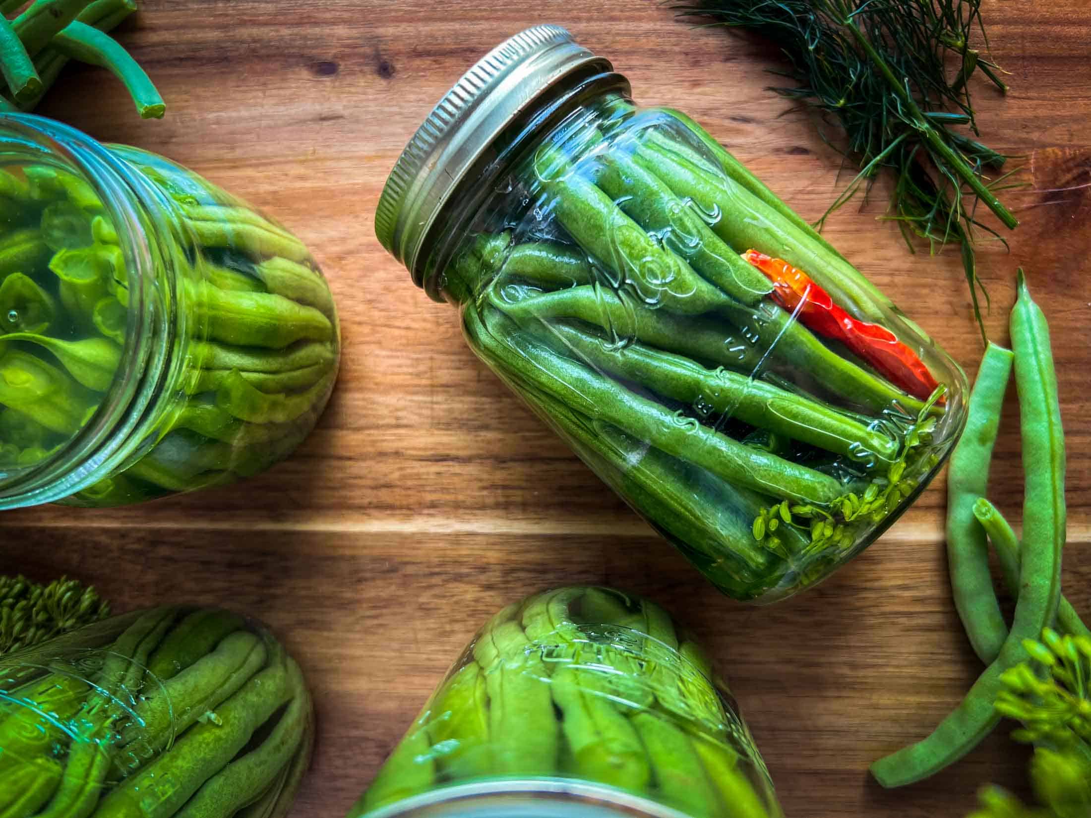 A prepared jar of fermented green beans tipped on its side on a wooden cutting board.
