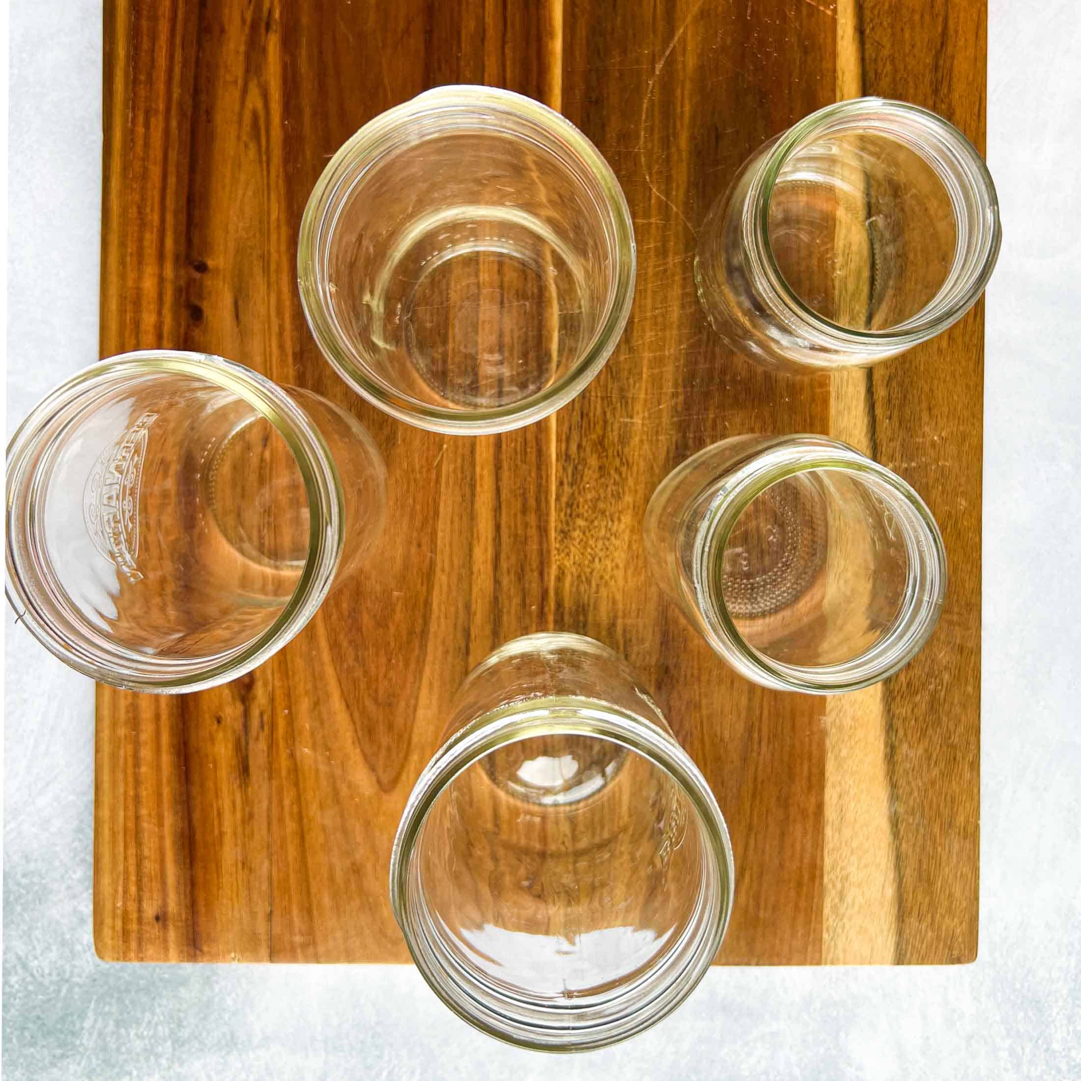 Five jars of varying sizes on a wooden cutting board.