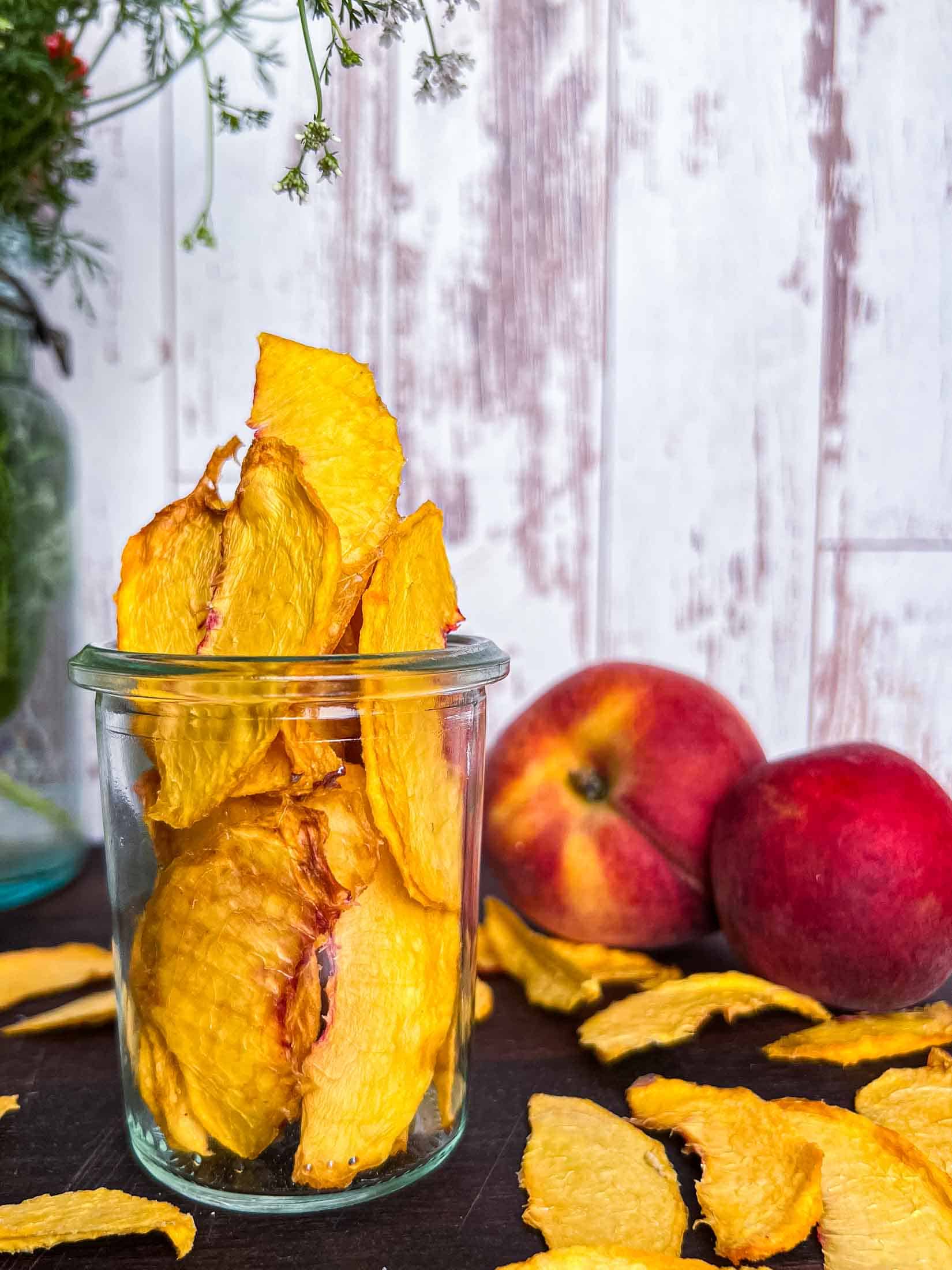 Dehydrated peaches in a glass weck jar with fresh and dried peaches in the foreground.