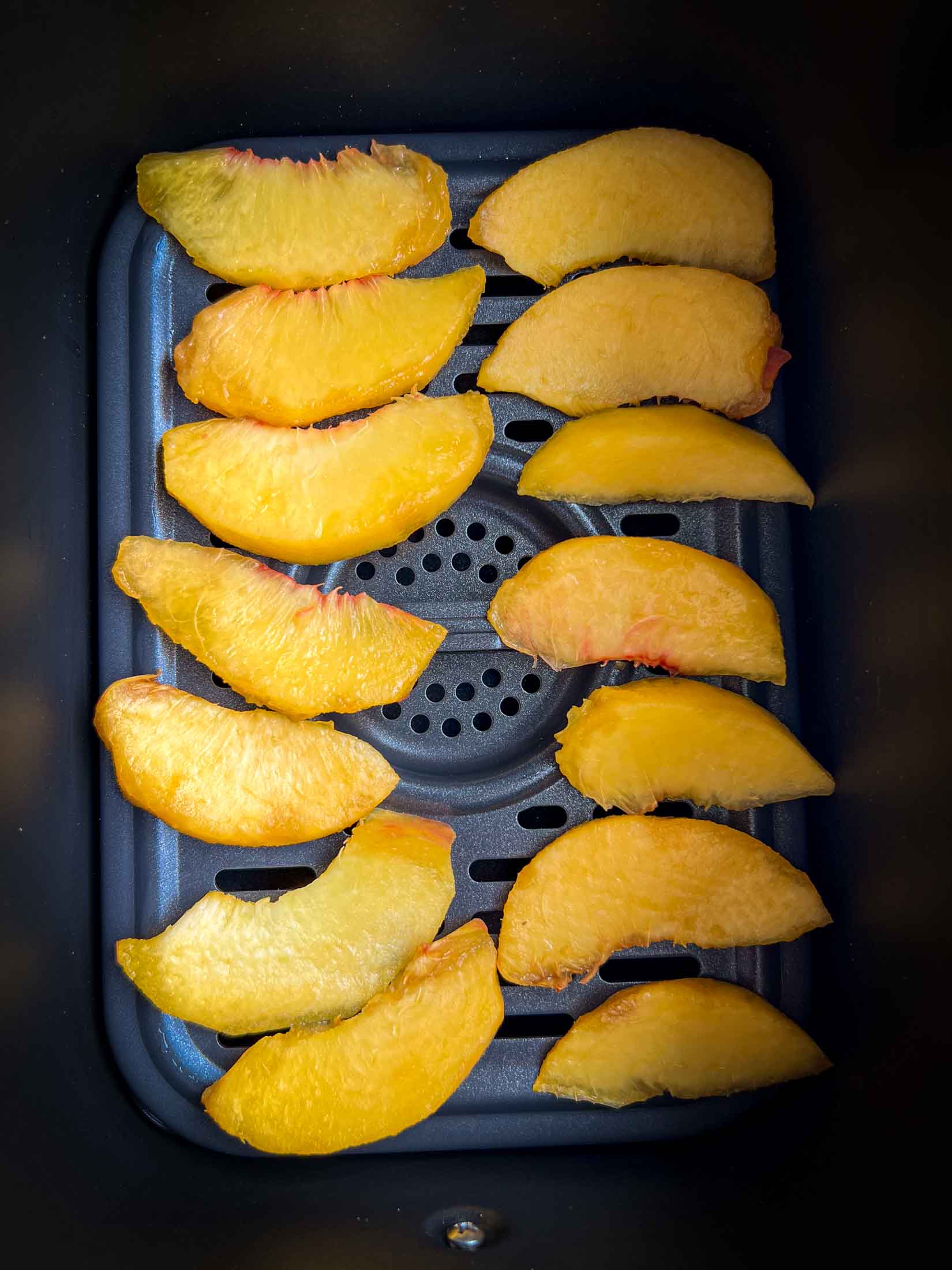 Fresh peaches arranged in an air fryer basket.
