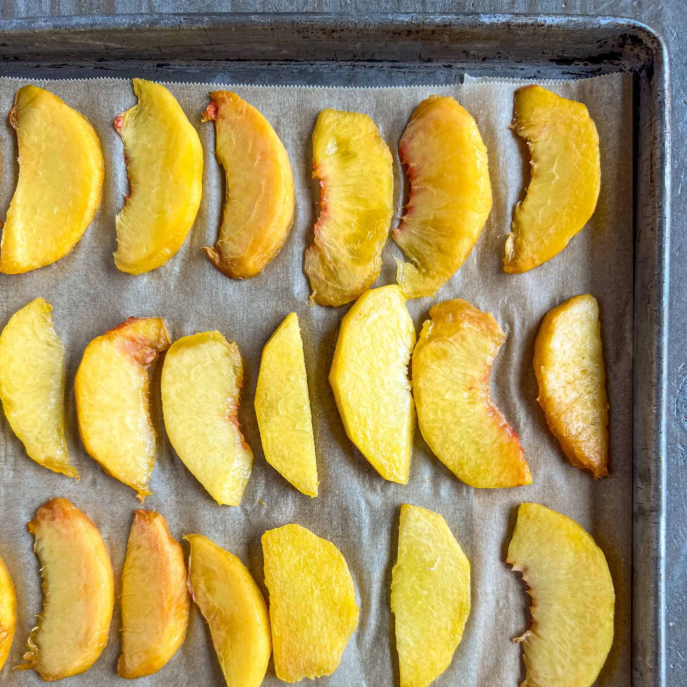 Fresh peaches on a piece of parchment paper on a baking sheet.