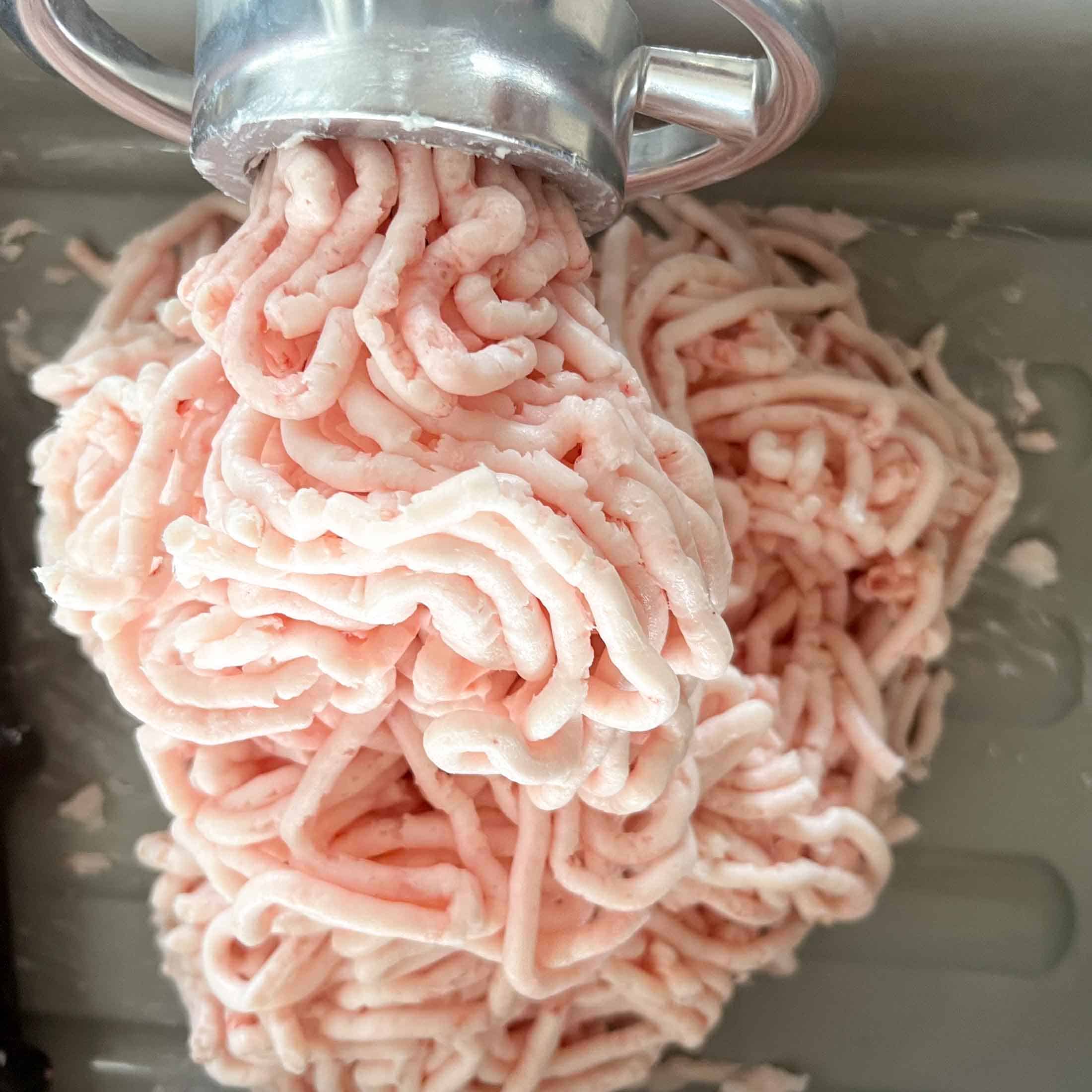 Ground pork lard coming out of the end of a meat grinder.