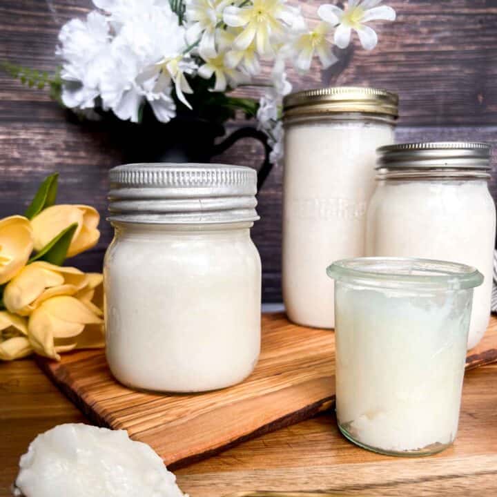 Rendered lard in glass jars with a large scoop of creamy fat on a gold spoon.