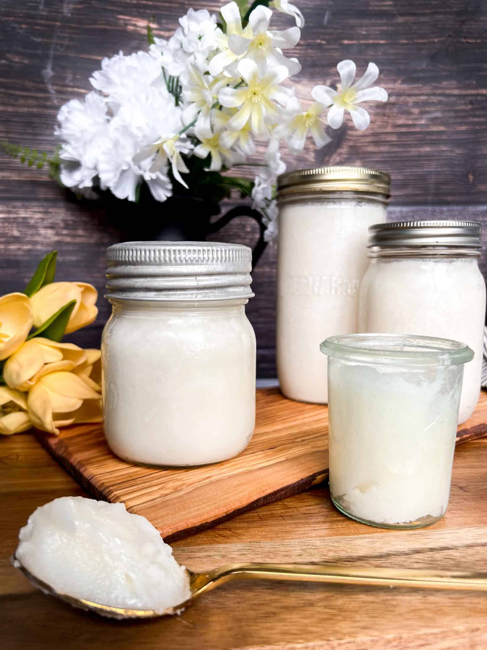 Rendered lard in glass jars with a large scoop of creamy fat on a gold spoon.