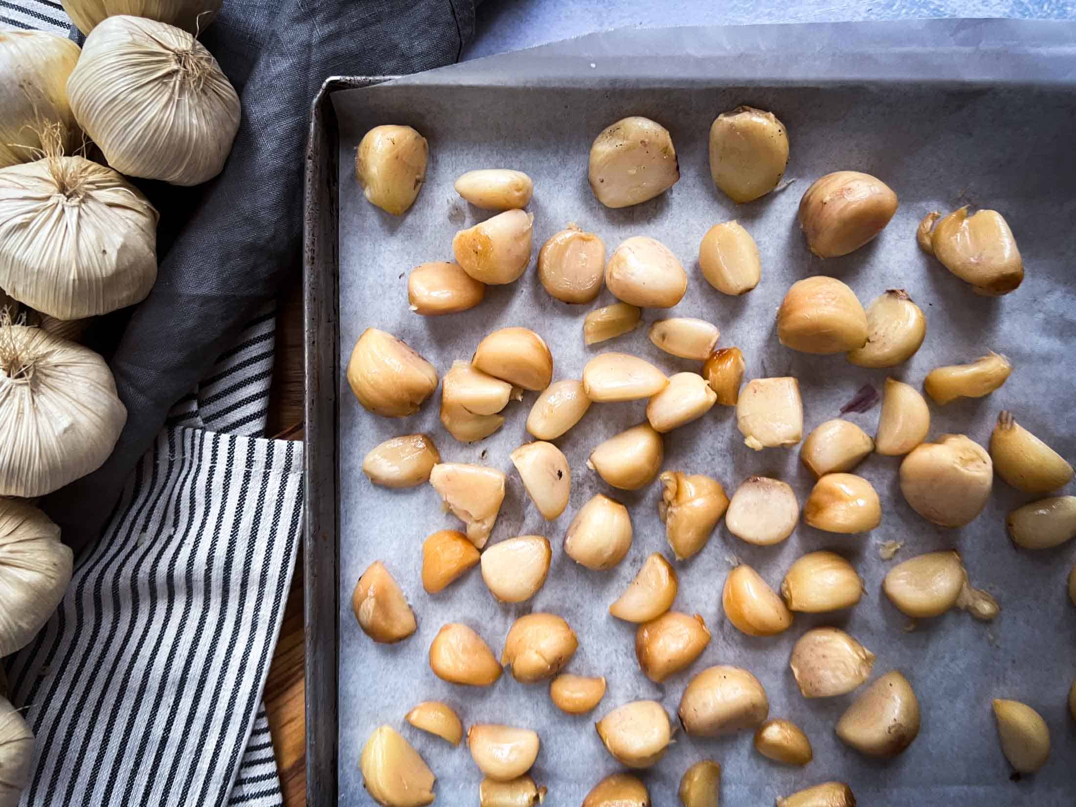 Peeled, smoked garlic cloves on a parchment lined baking sheet.