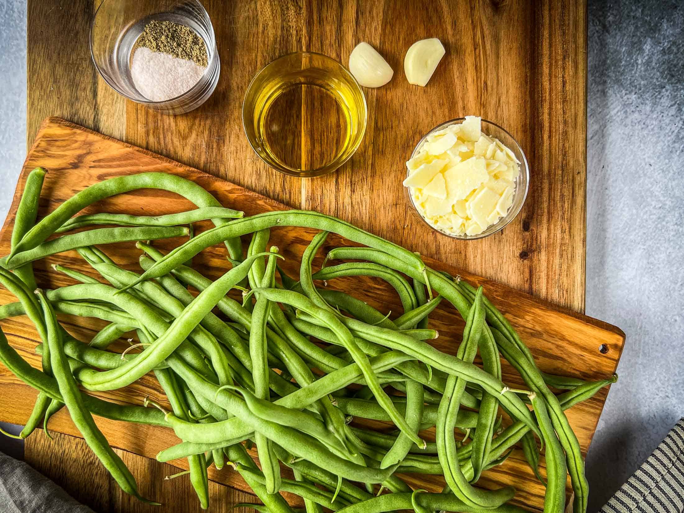 Key ingredients for smoked green beans including beans, parmesan, salt and pepper, two garlic cloves, and olive oil.