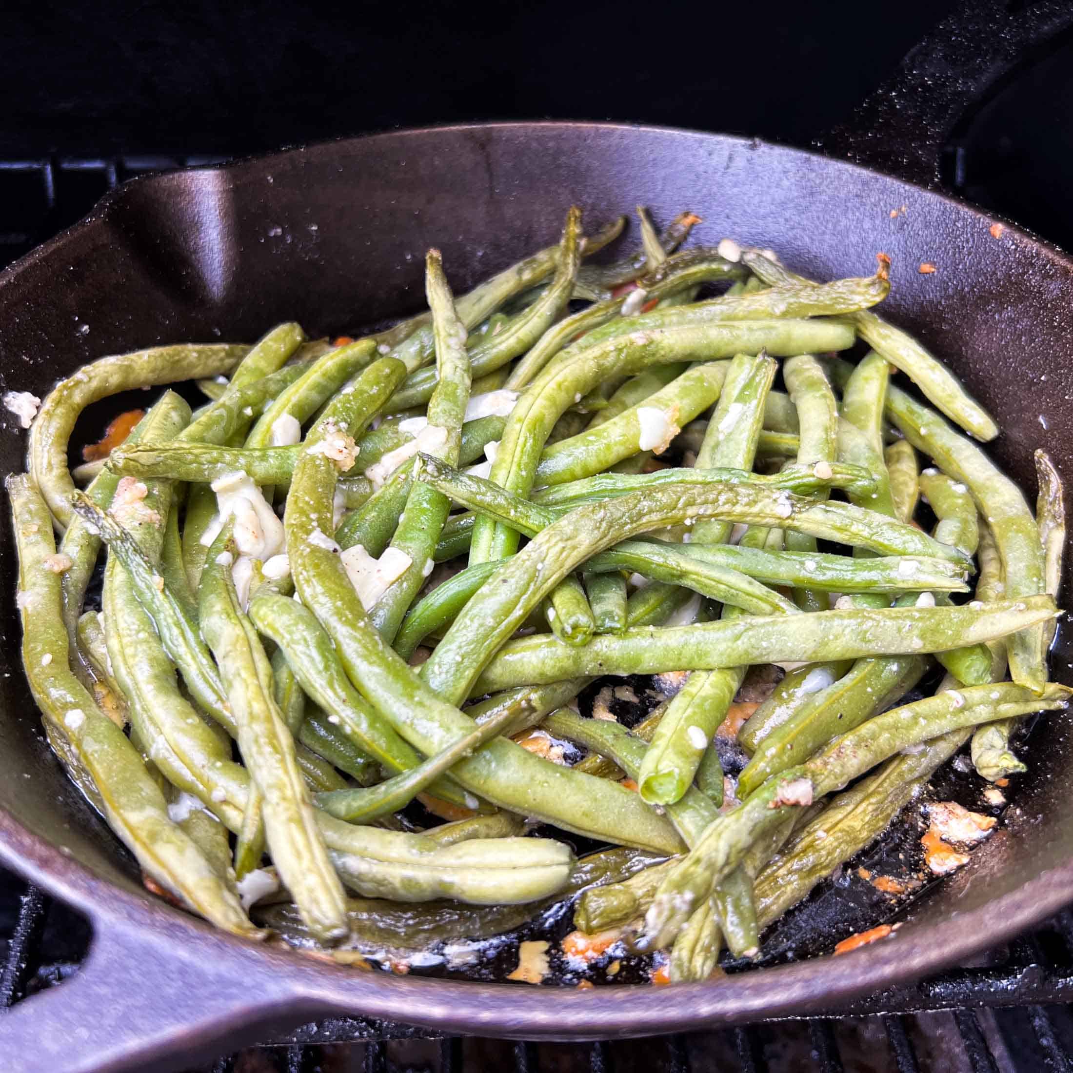 Fully smoked green beans on a cast iron pan showing parmesan flakes.
