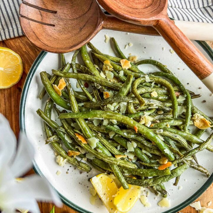 Smoked green beans on a ceramic plate sprinkled with parmesan, pepper, salt, and lemon wedges.