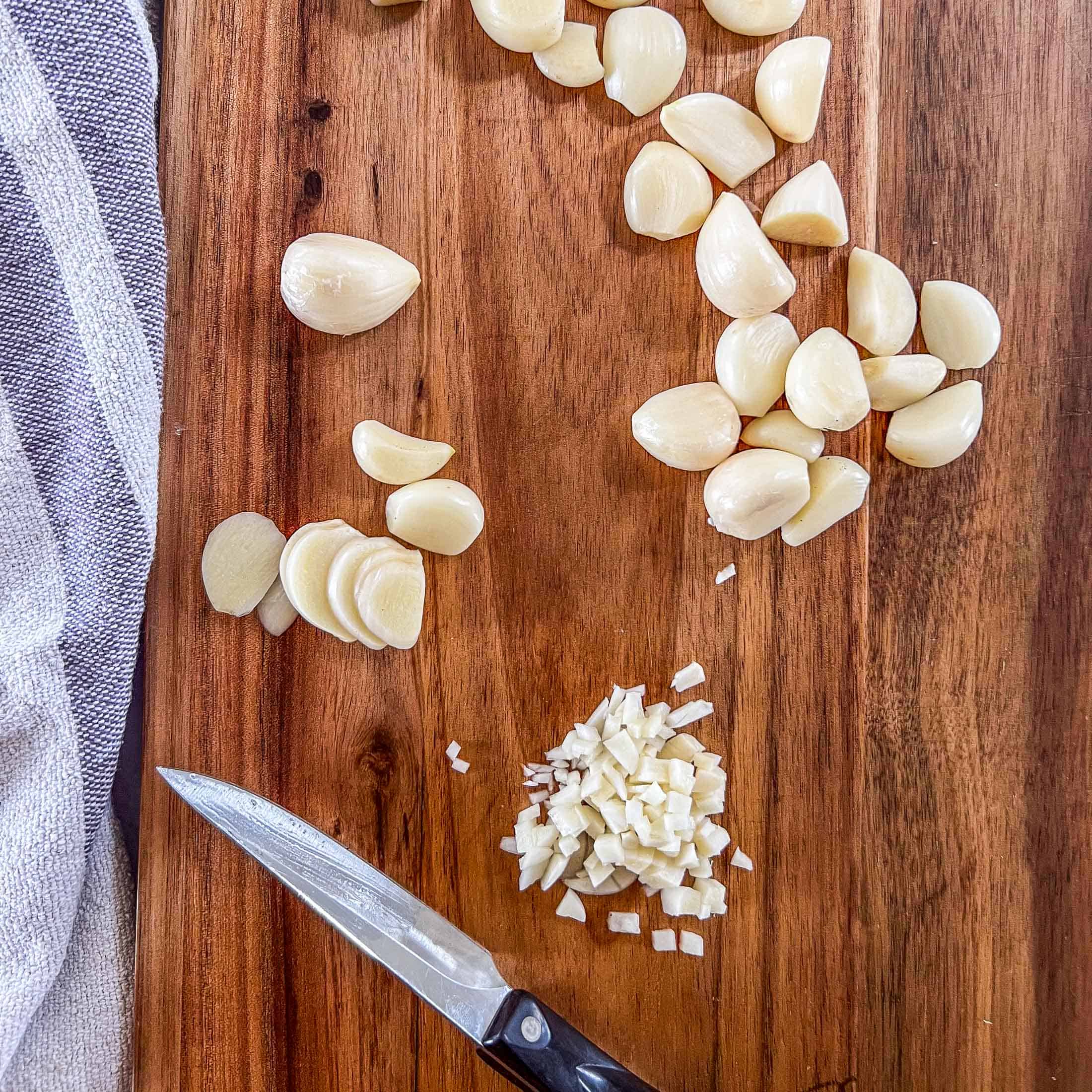 Slices of raw garlic and small pieces of garlic on a wooden cutting board.