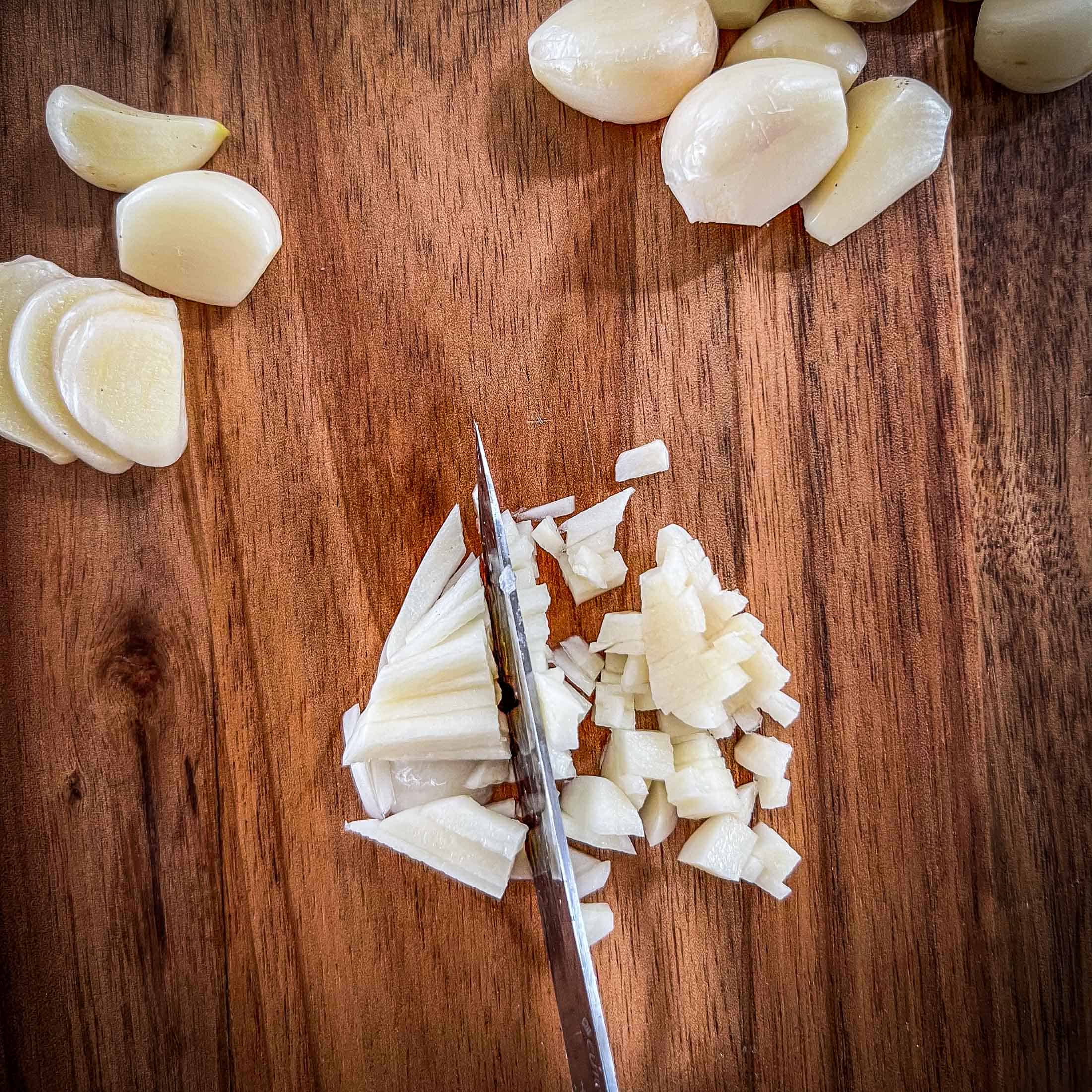 Finely mincing a raw clove of garlic with a sharp knife.