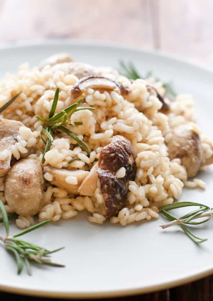 Mushroom risotto on a white plate with fresh green herbs.