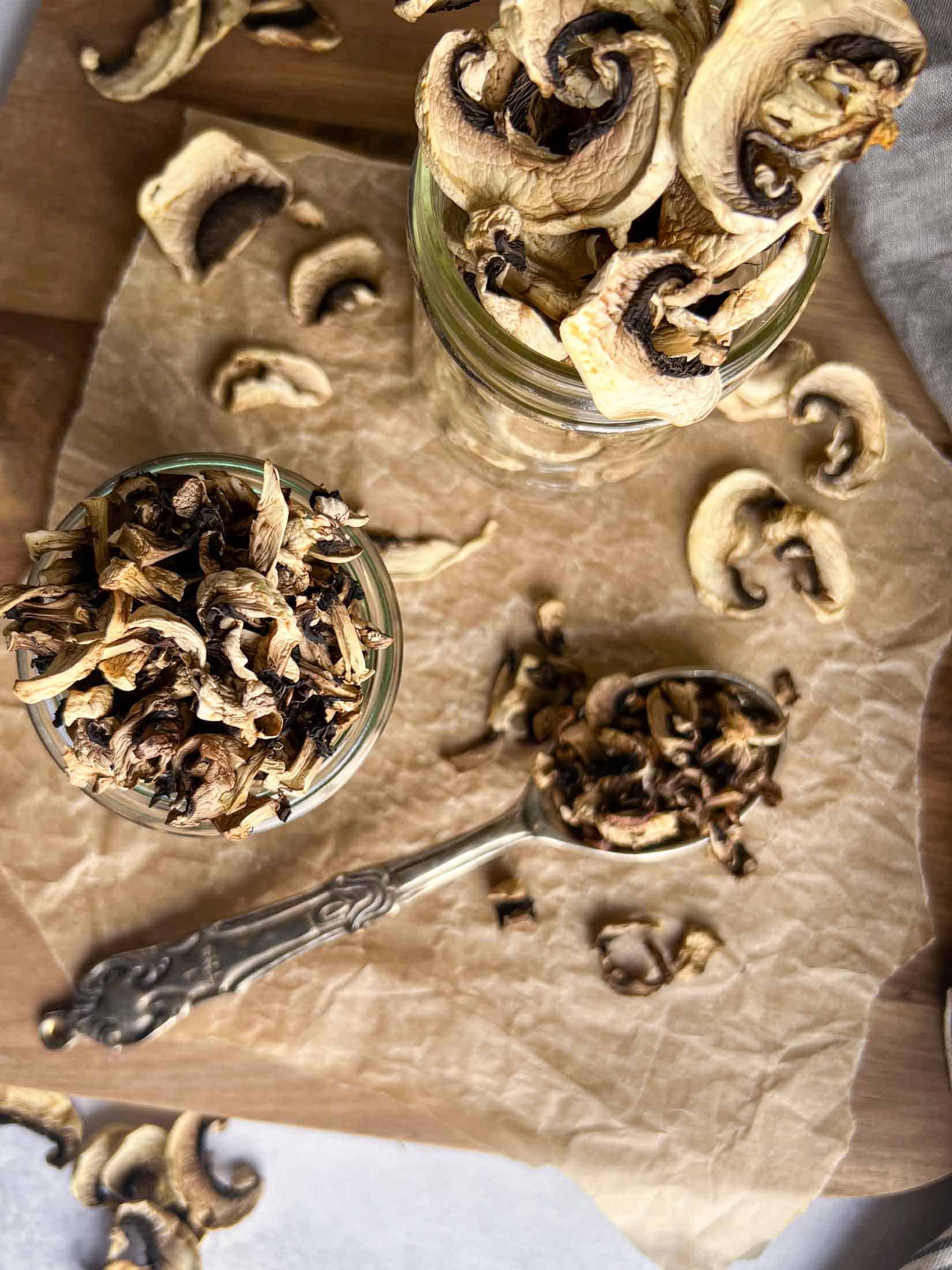Dried mushrooms spilling out of a glass jar and heaping out of a silver spoon.
