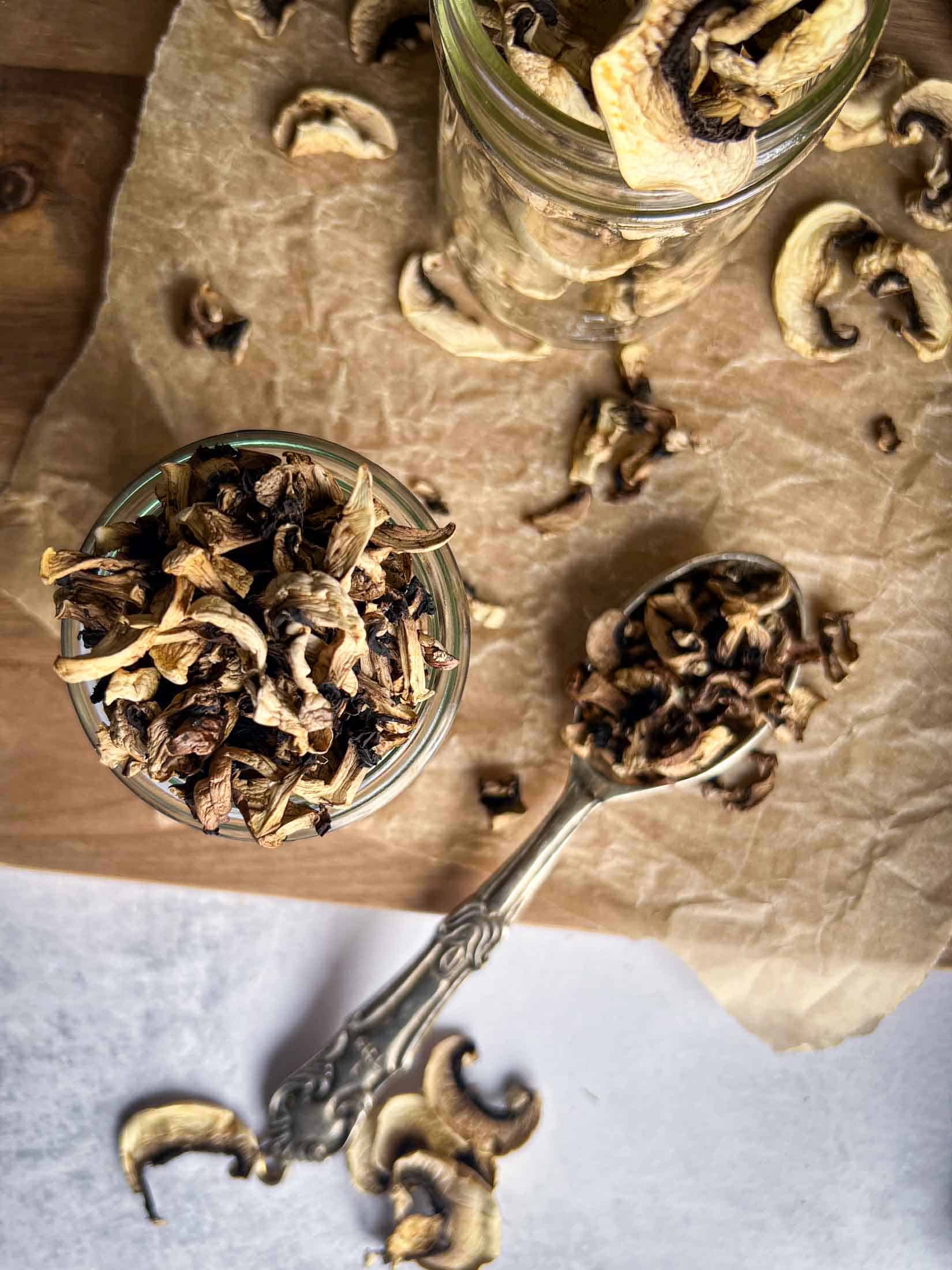 Dried mushrooms spilling out of a glass jar and heaping out of a silver spoon.