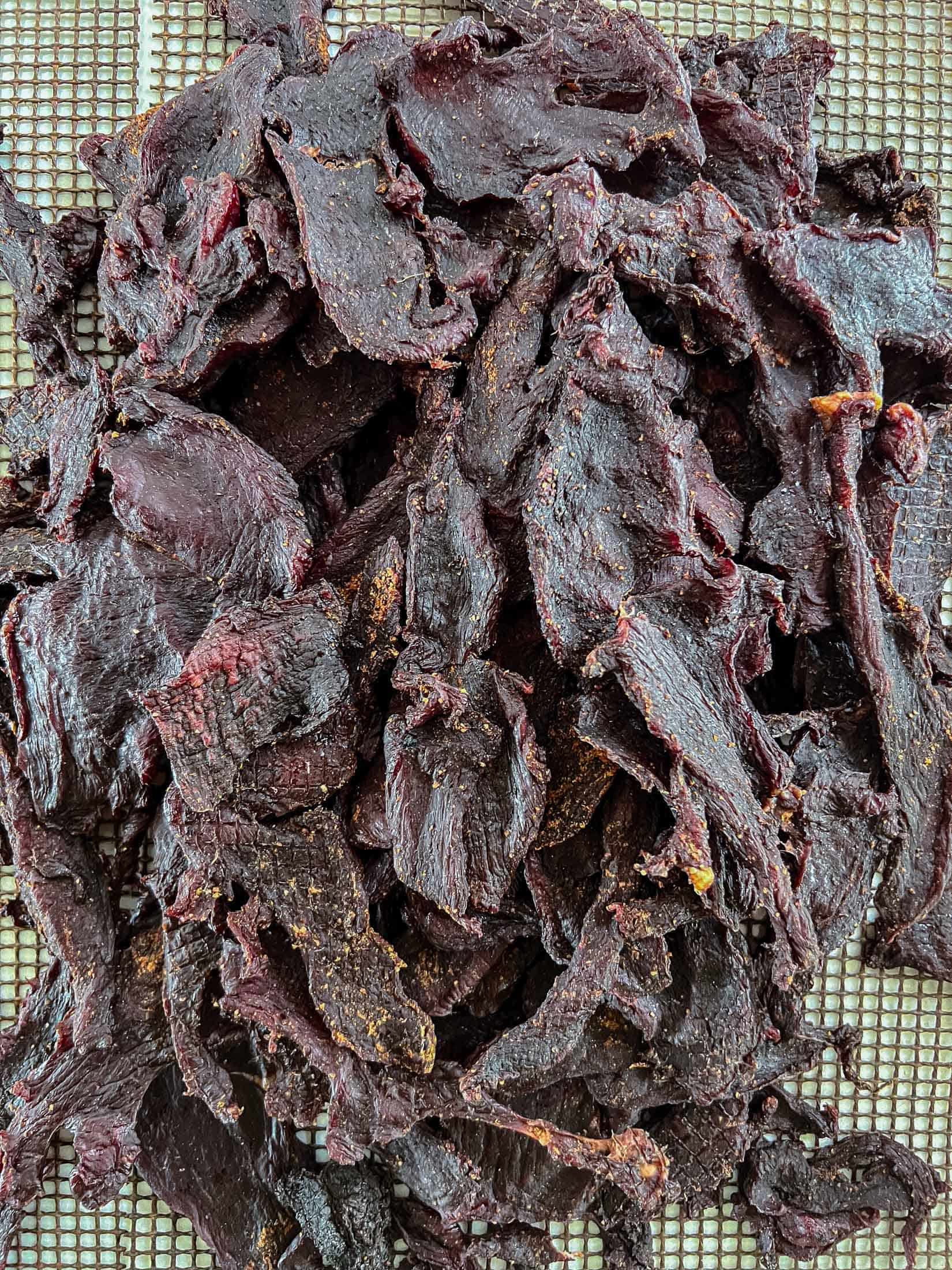 Fully cooked venison jerky piled high showing deep, dark red chunks.