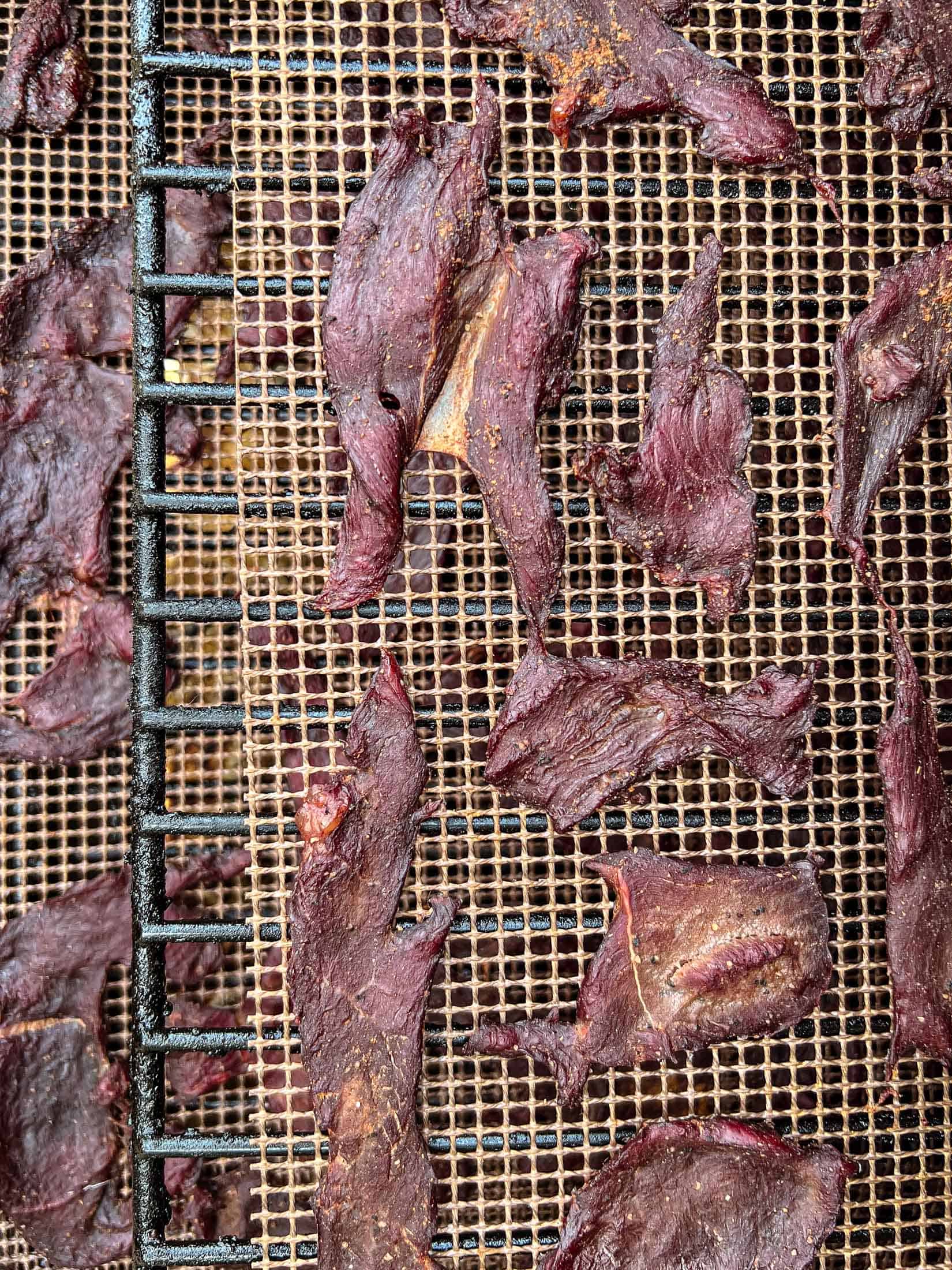 Fully cooked venison jerky on a grill mat on a pellet grill.