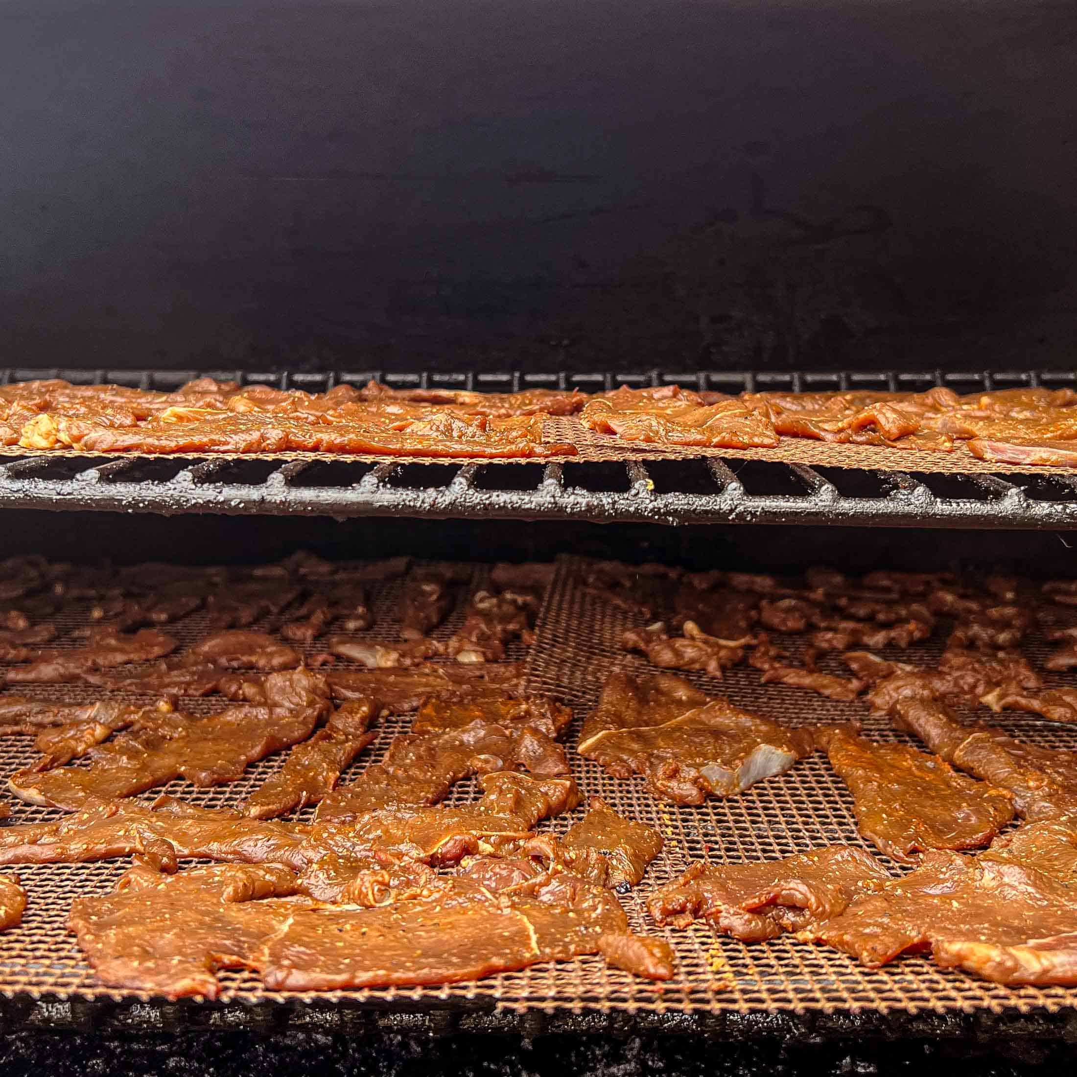 Raw, sliced venison jerky sitting on grill mats inside of a Traeger pellet grill.