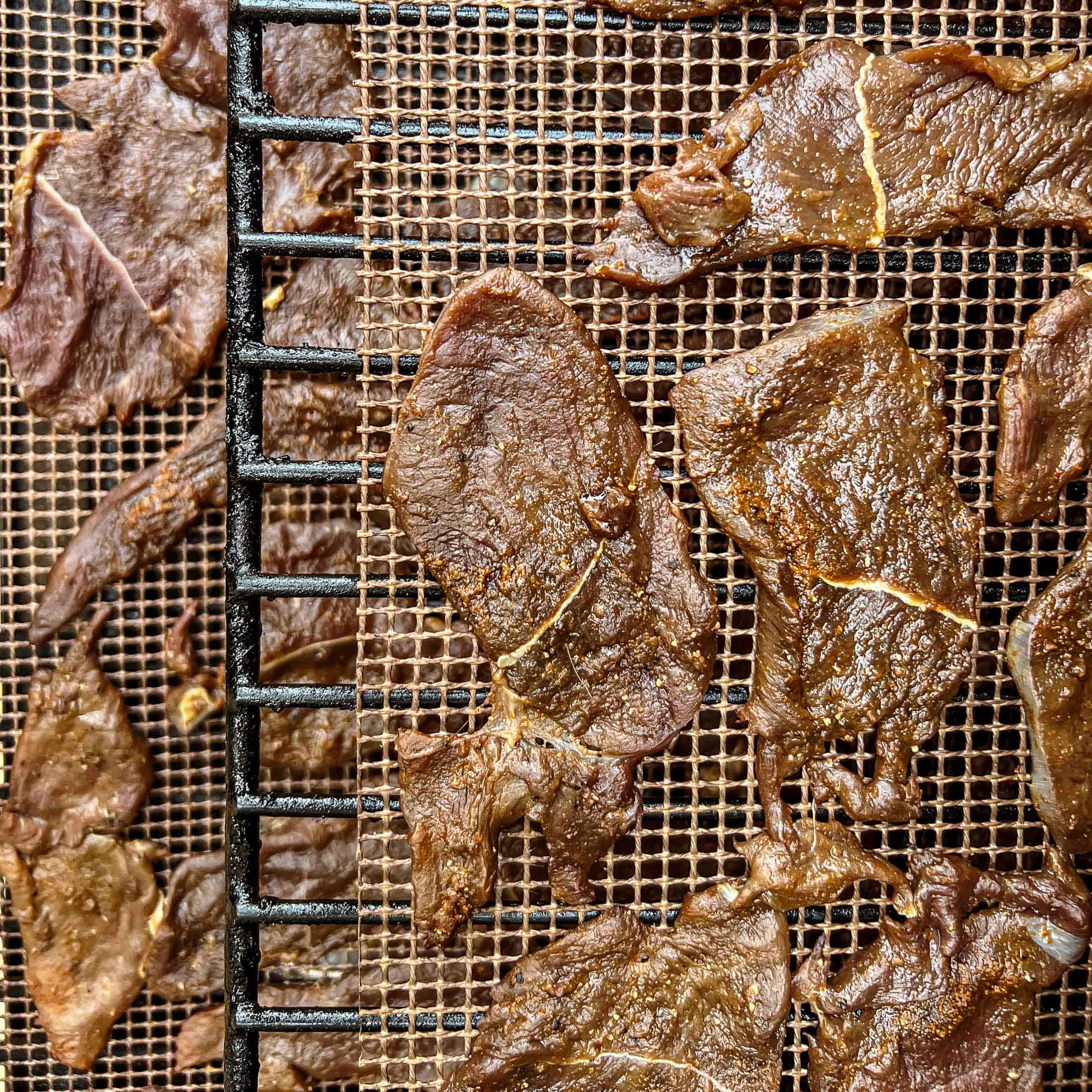 An overhead view of raw venison jerky on the smoker.