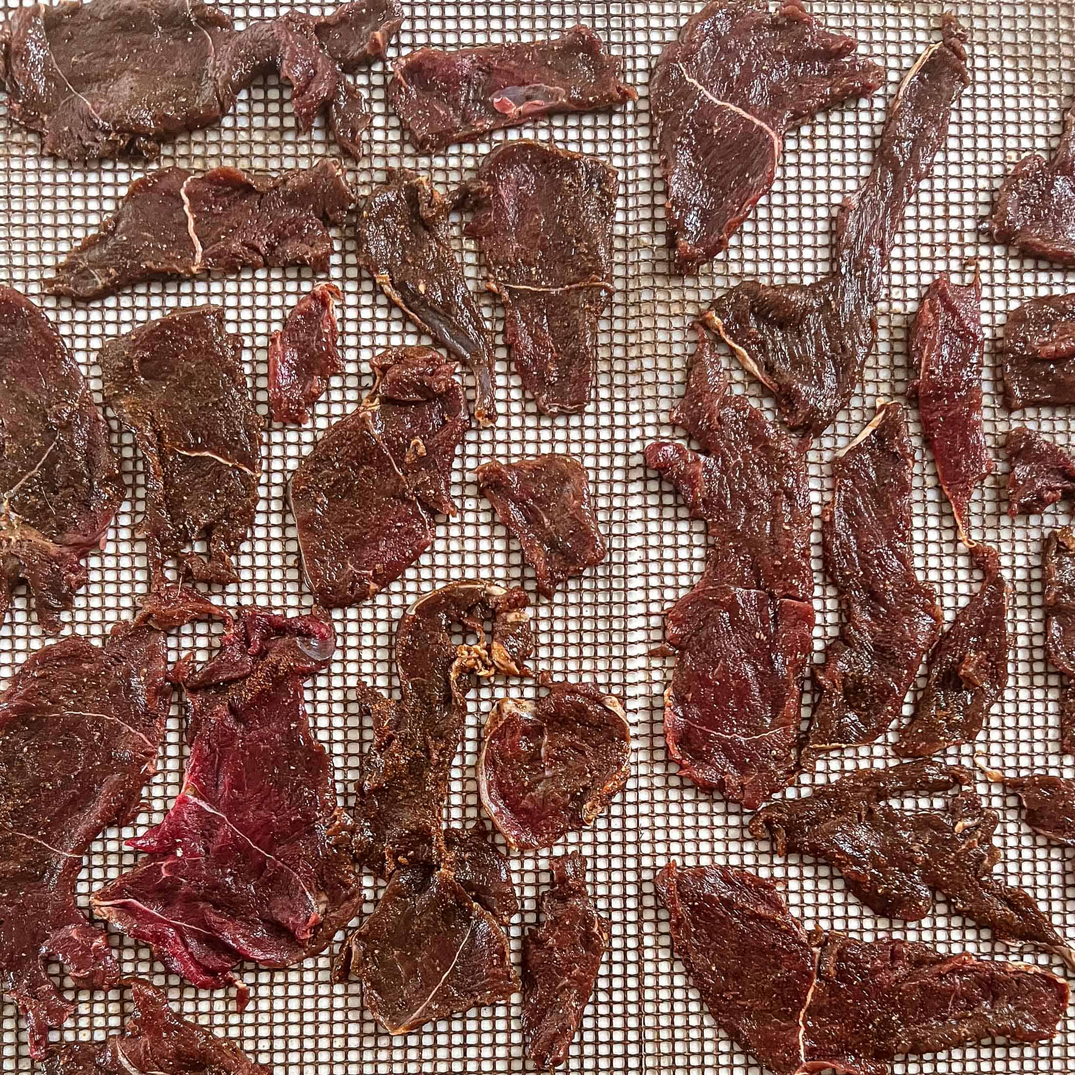 Raw sliced of venison jerky on a grill mat.