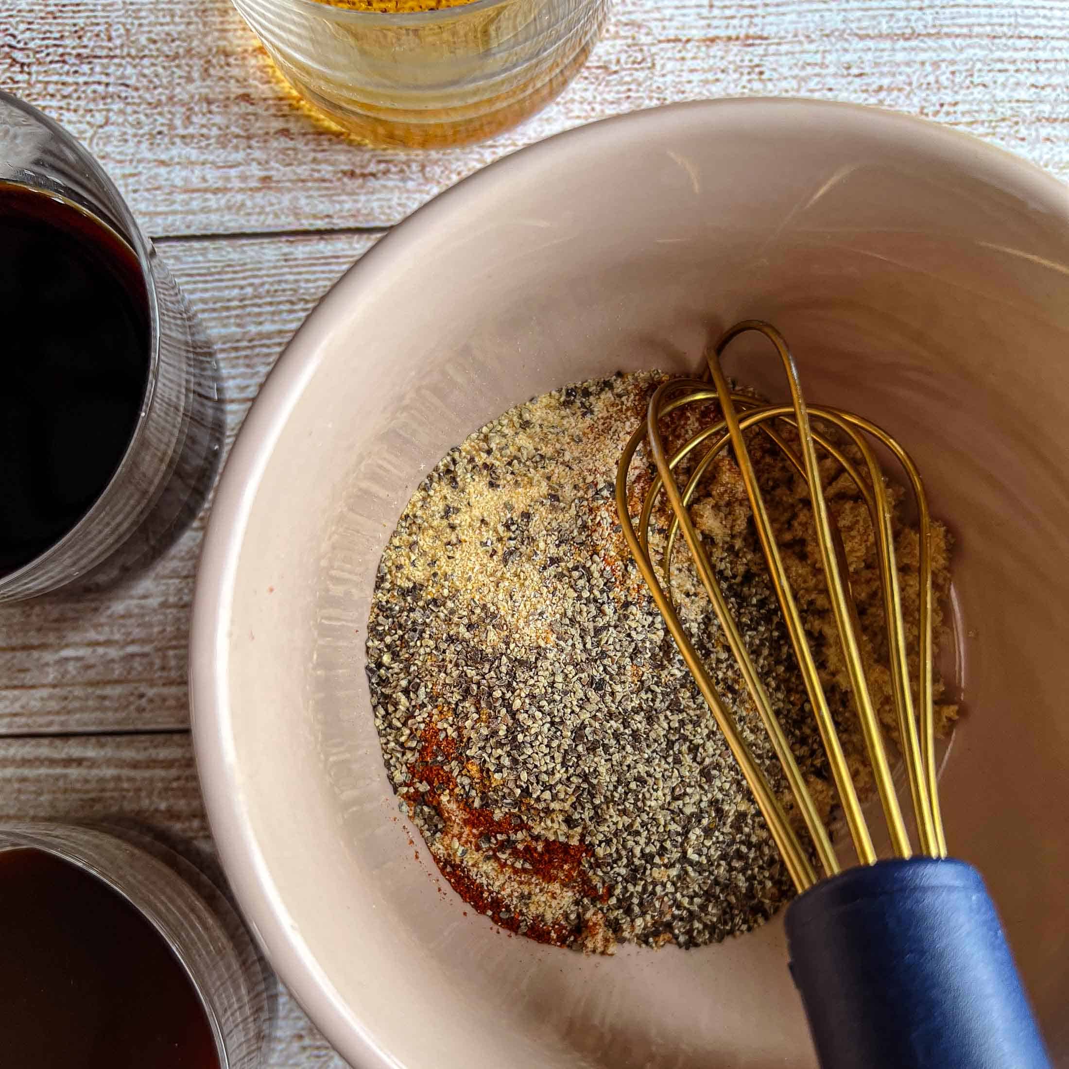 A golden whisk mixing dry ingredients in a small bowl.