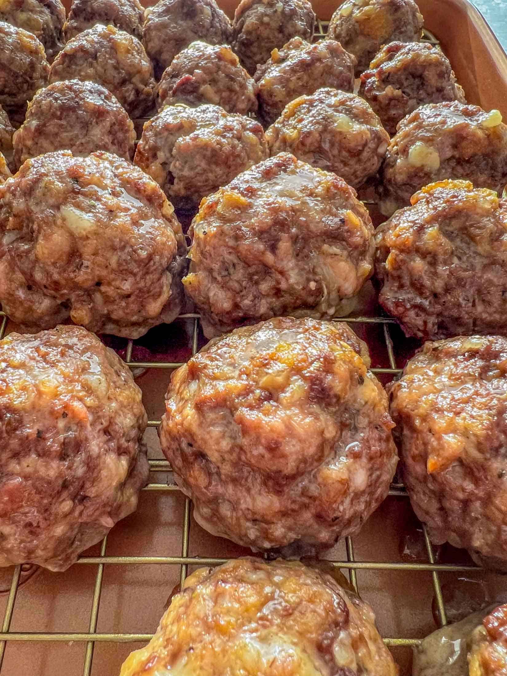 Fully cooked meatballs on a wire cooling rack inside of a baking sheet.