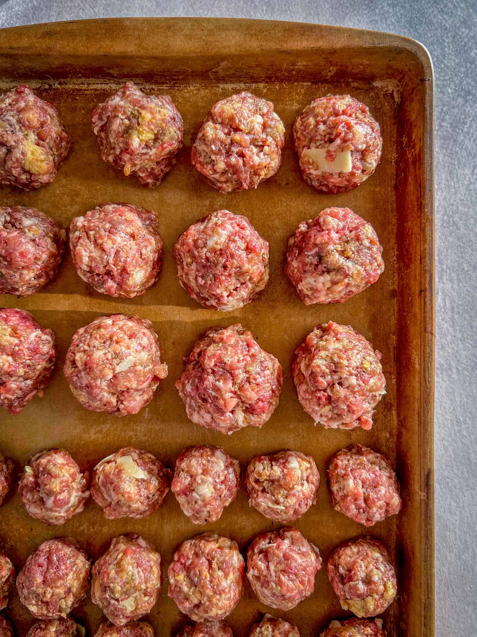 A mixture of large and small venison meatballs on a cookie sheet.