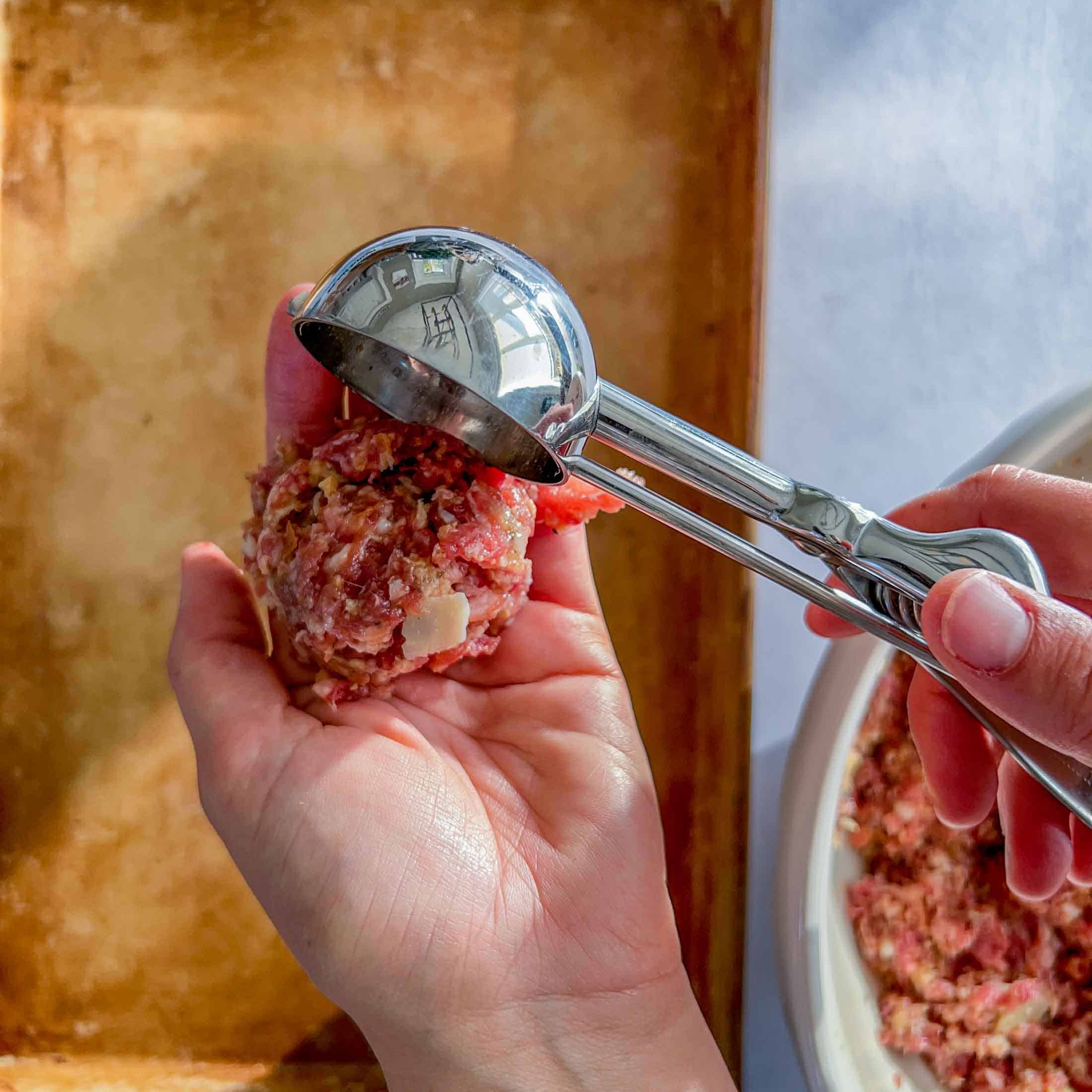 Meatball mixture being dropped into an open palm.