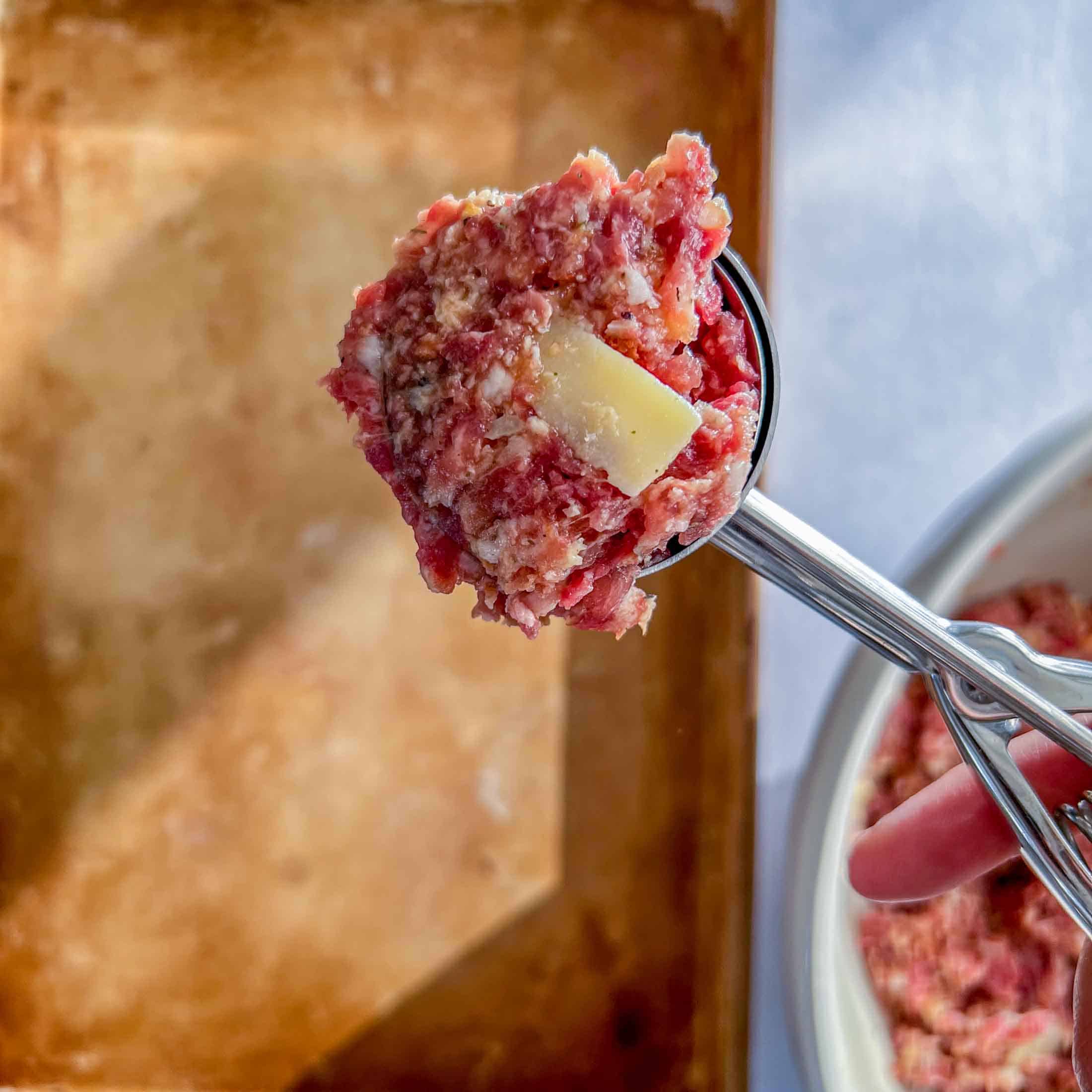 A large cookie scoop full of raw meatball mixture.