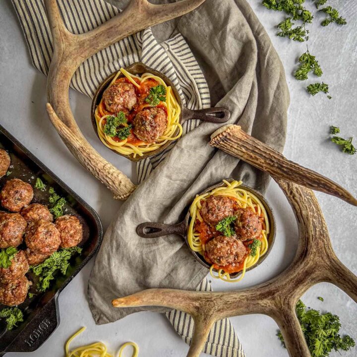 Venison meatballs in small cast iron pans with deer antlers surrounding them.