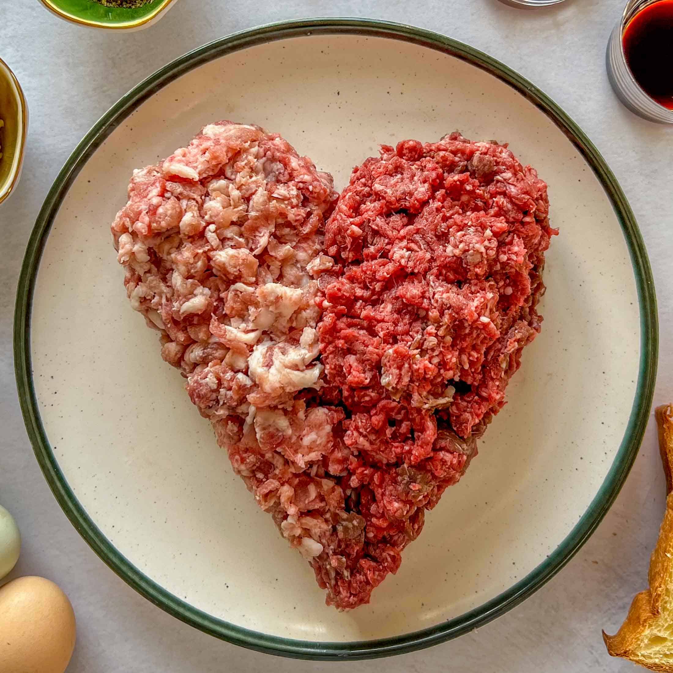 Ground pork and ground venison shaped into a heart on a green rimmed stone wear plate.