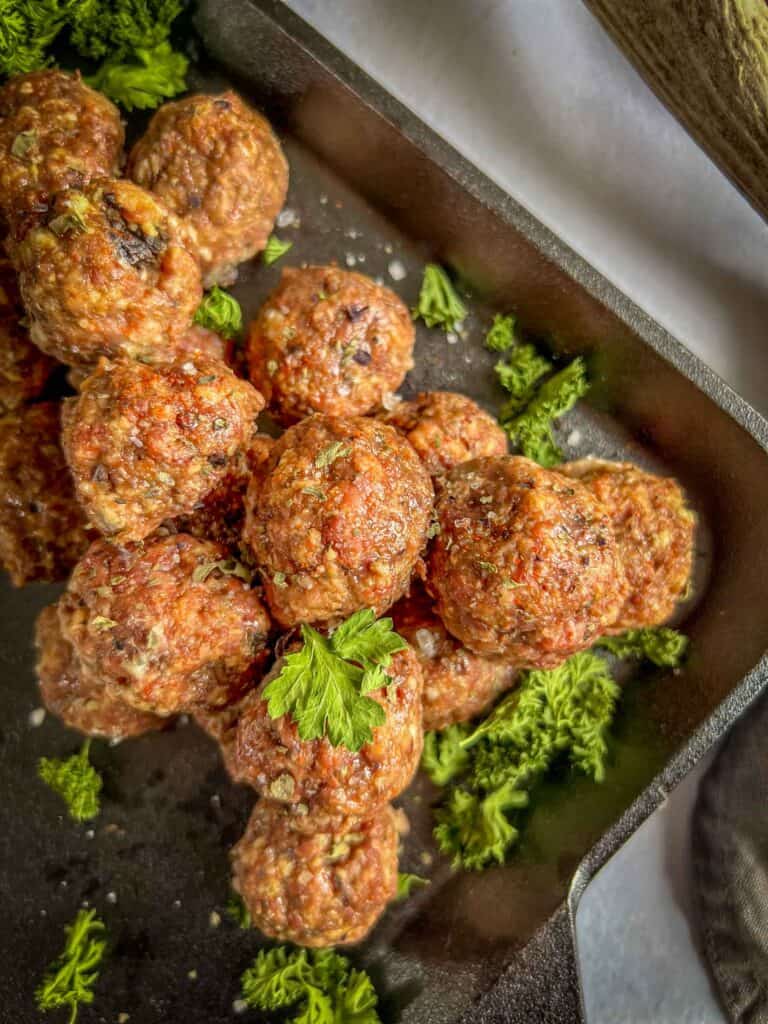 A closeup view of freshley cooked meatballs on a square cast iron skillet with parsley as garnish.