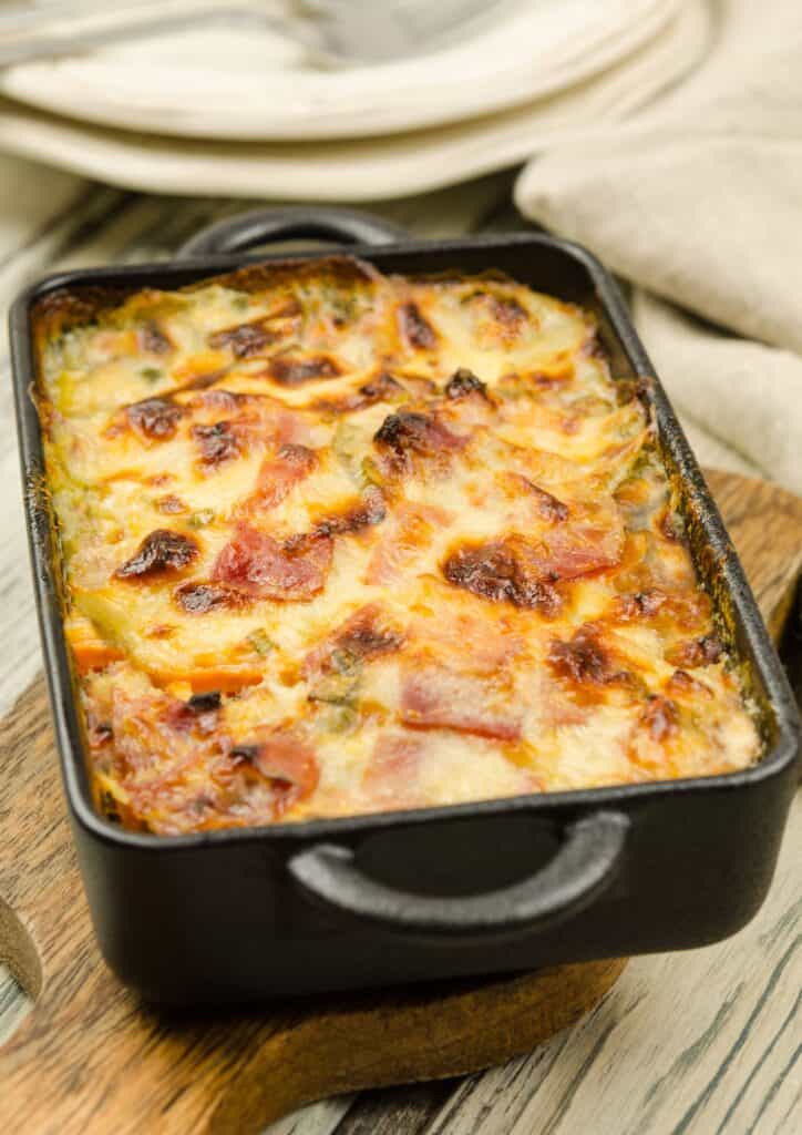 Cheesy scalloped potatoes with ham on top in a dark casserole dish.
