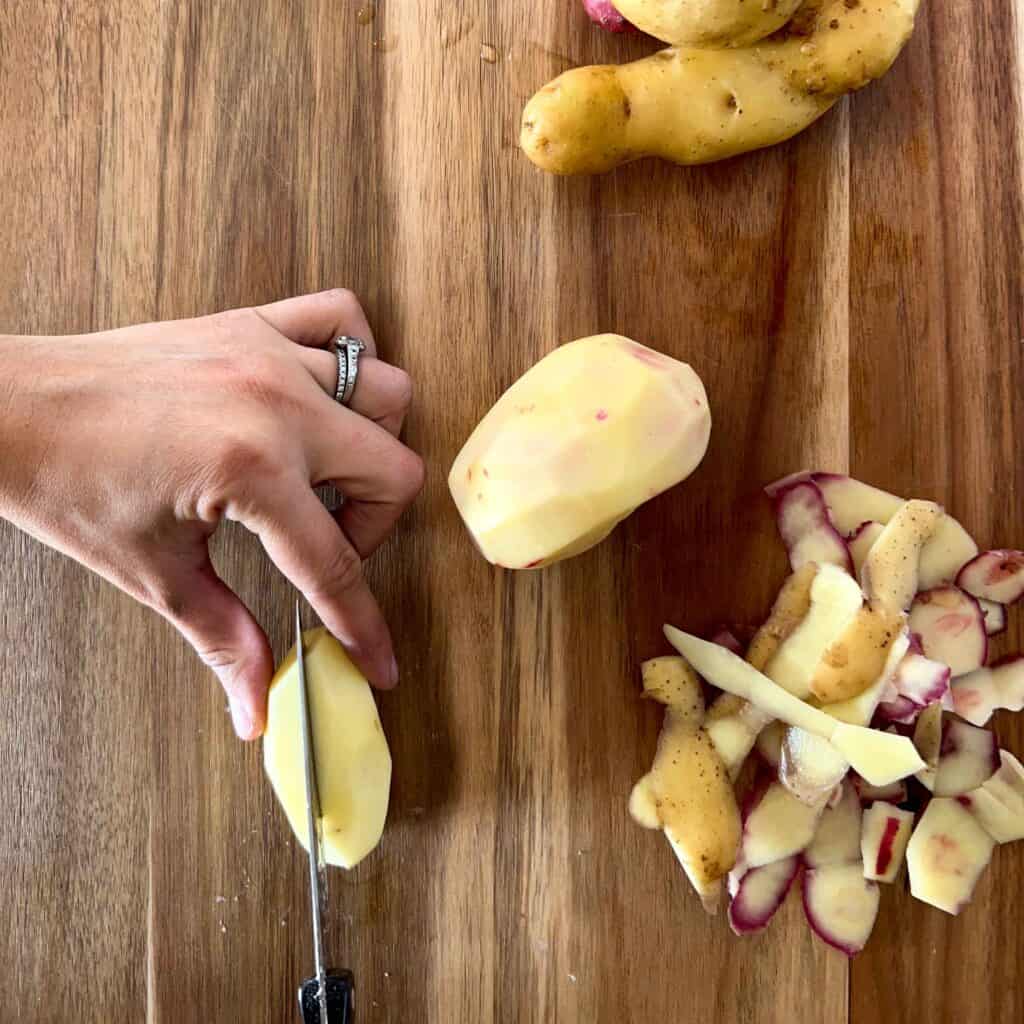 A peeled potato being sliced in half.