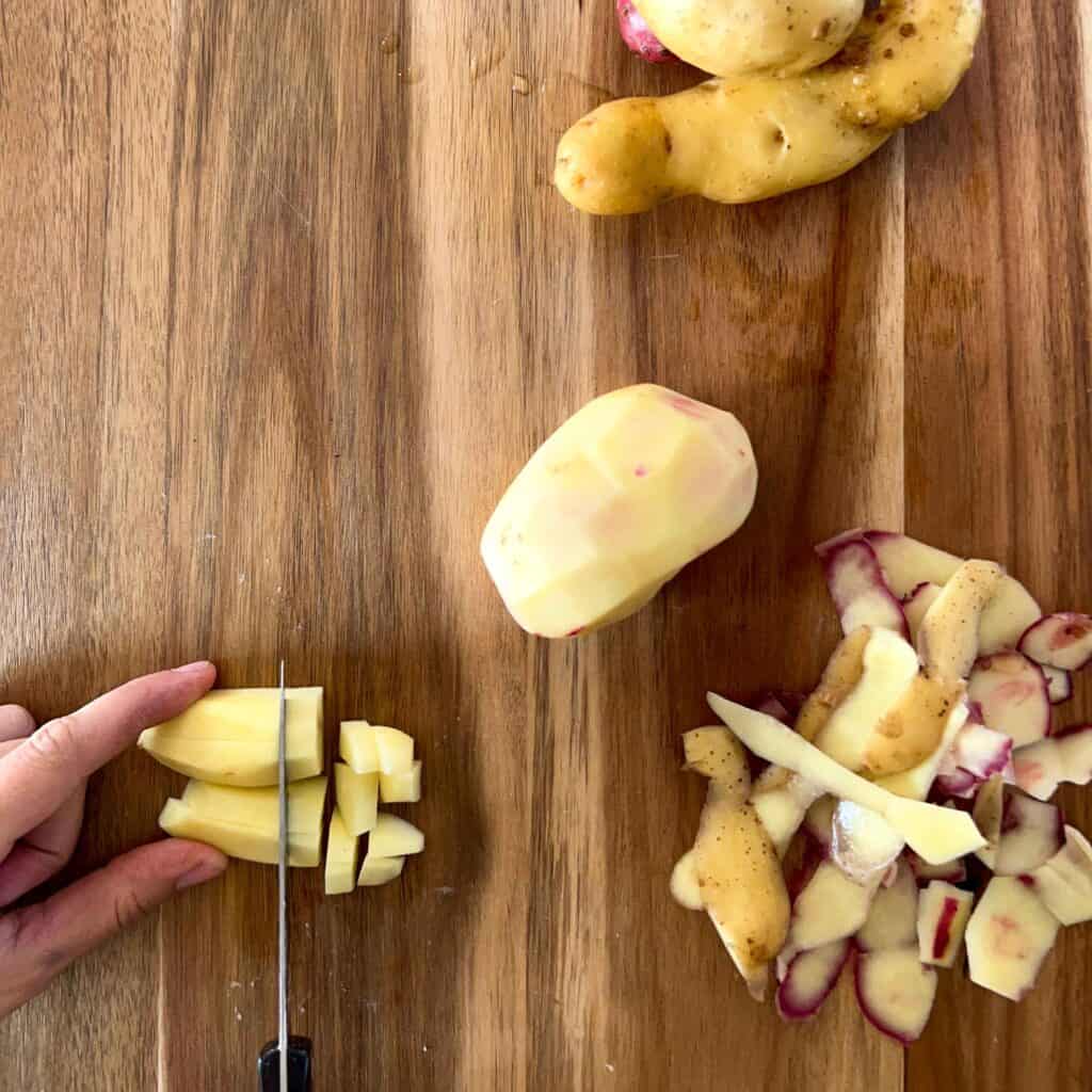 A peeled potato being cubed on a wooden cutting board.