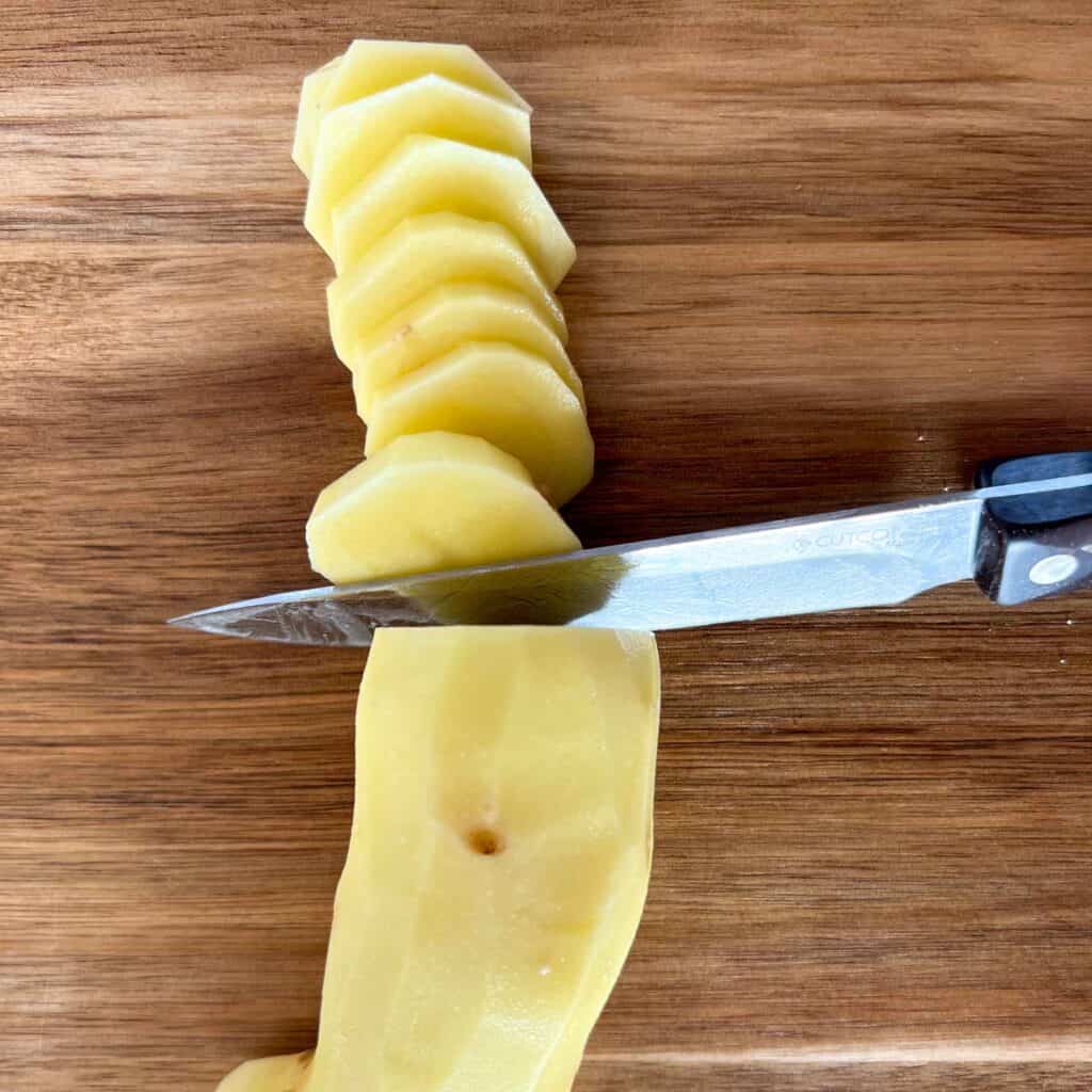 A peeled potato being cut into thin slices.