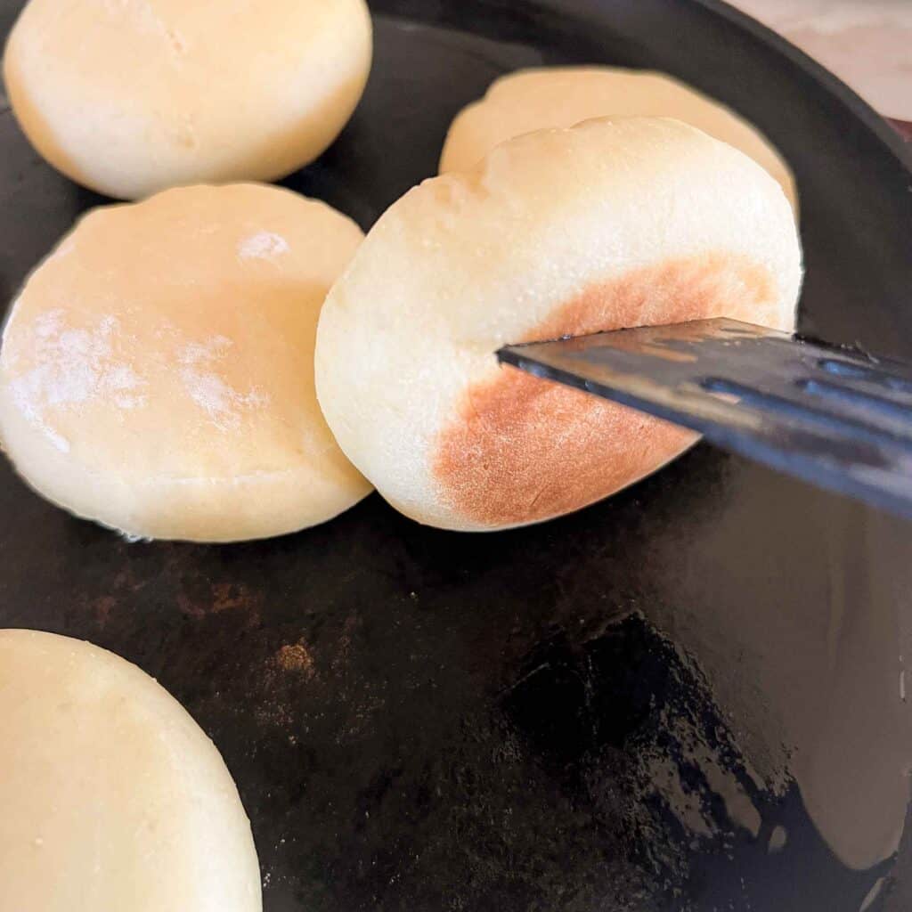 An english muffin being turned over with a spatula revealing a perfectly golden brown base.