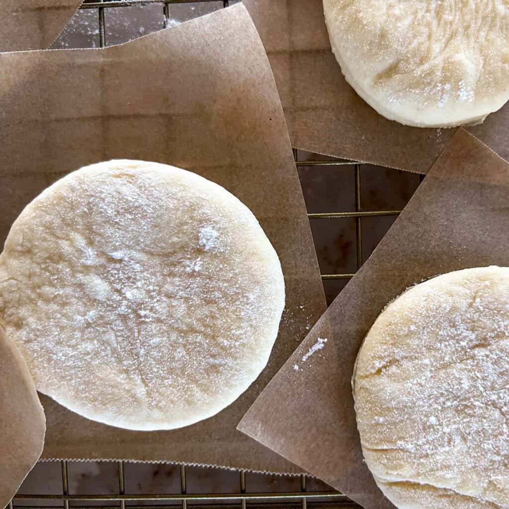 Freshly cut english muffins rising on squares of parchment.