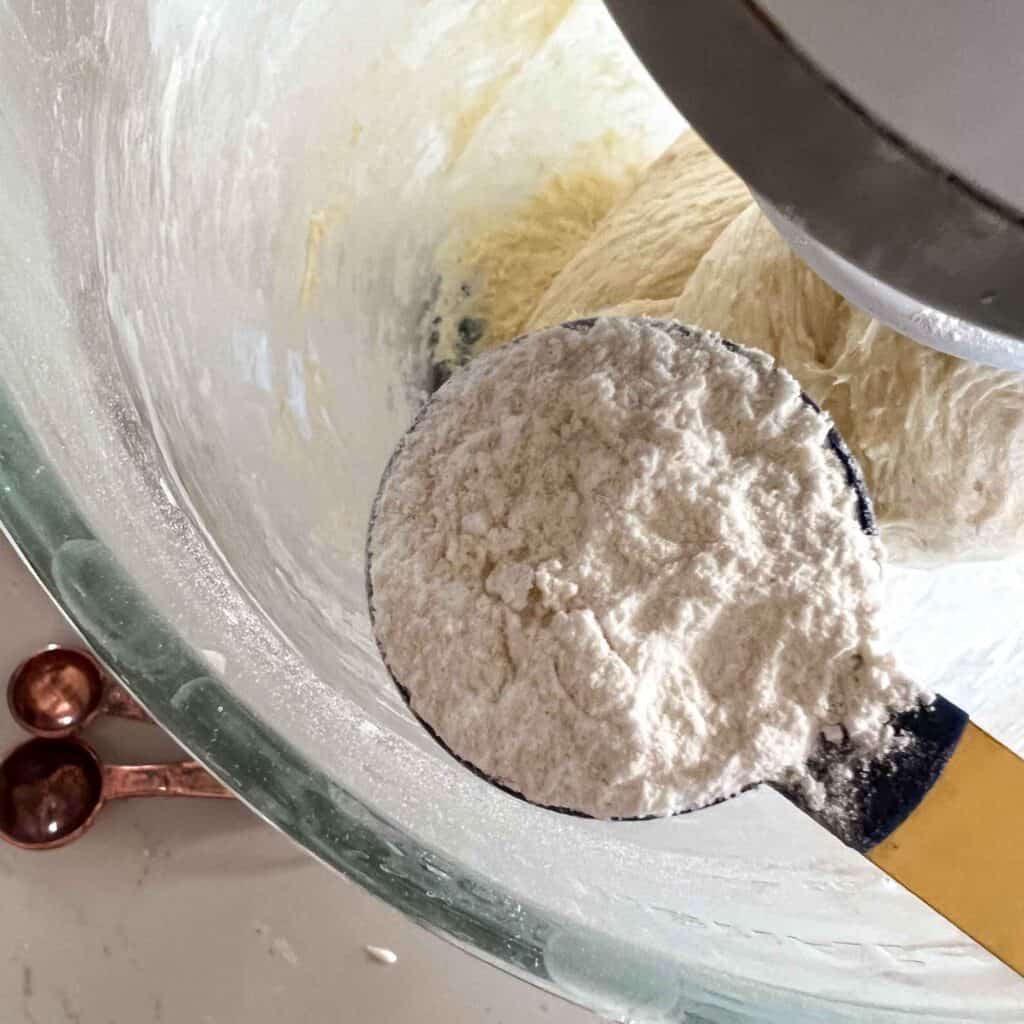 Flour being added to sticky sourdough in a mixing bowl.
